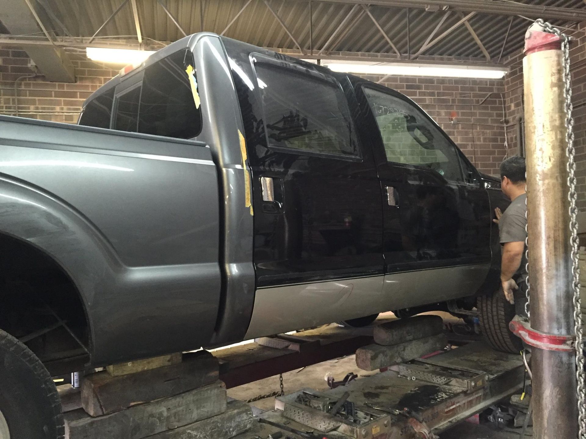 Truck in auto shop, being worked on; gray and black paint, person by the door.