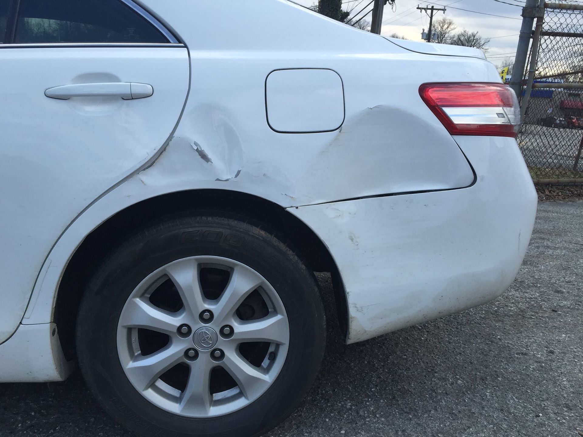 White car with significant damage to the rear quarter panel, near the fuel door.