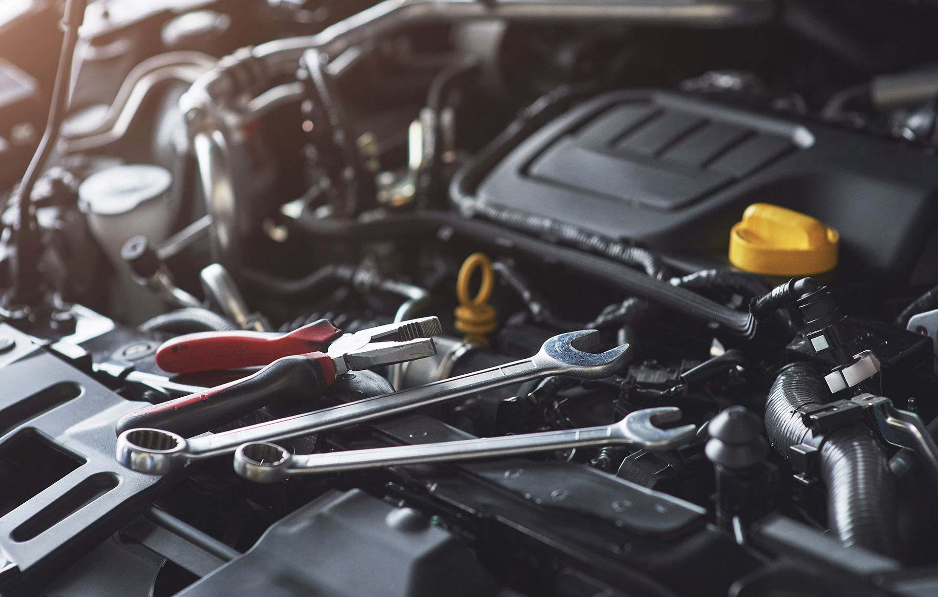 Wrench tools on an open car engine. Red and silver tools, black engine components.