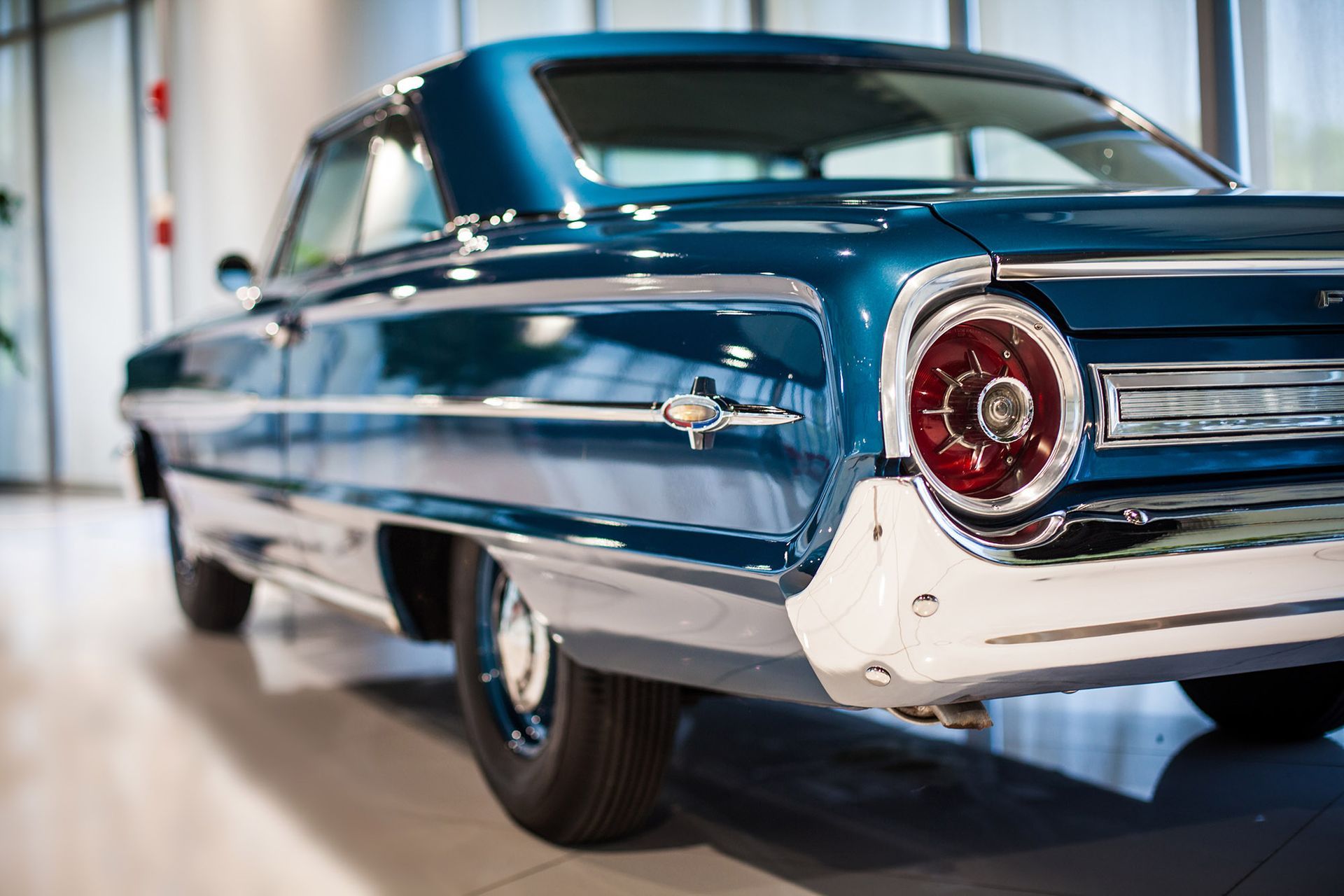 Blue classic car, rear view, in a showroom, chrome details, round taillight.