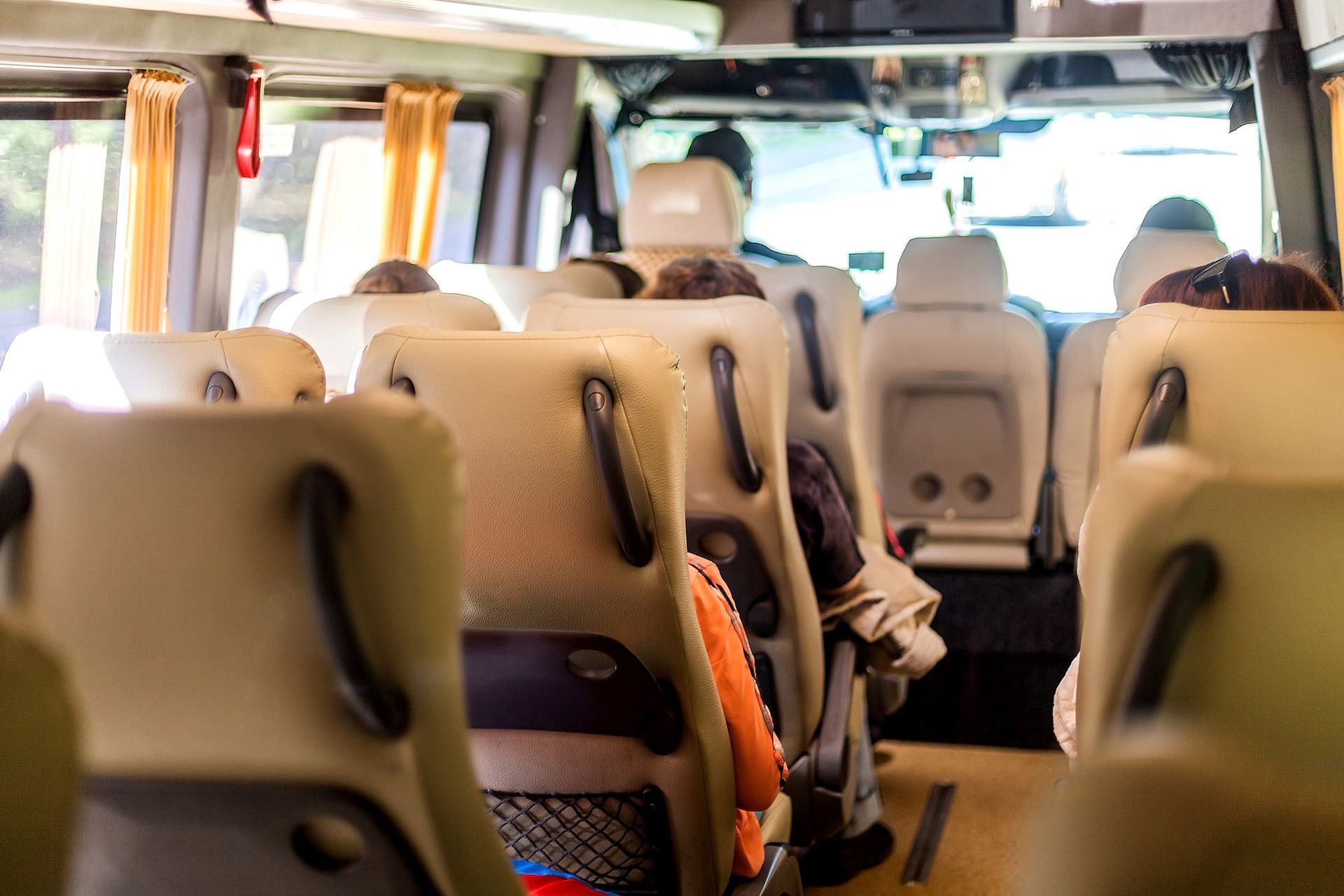 Interior of a passenger van with beige seats, some occupied, and a driver visible in the front.