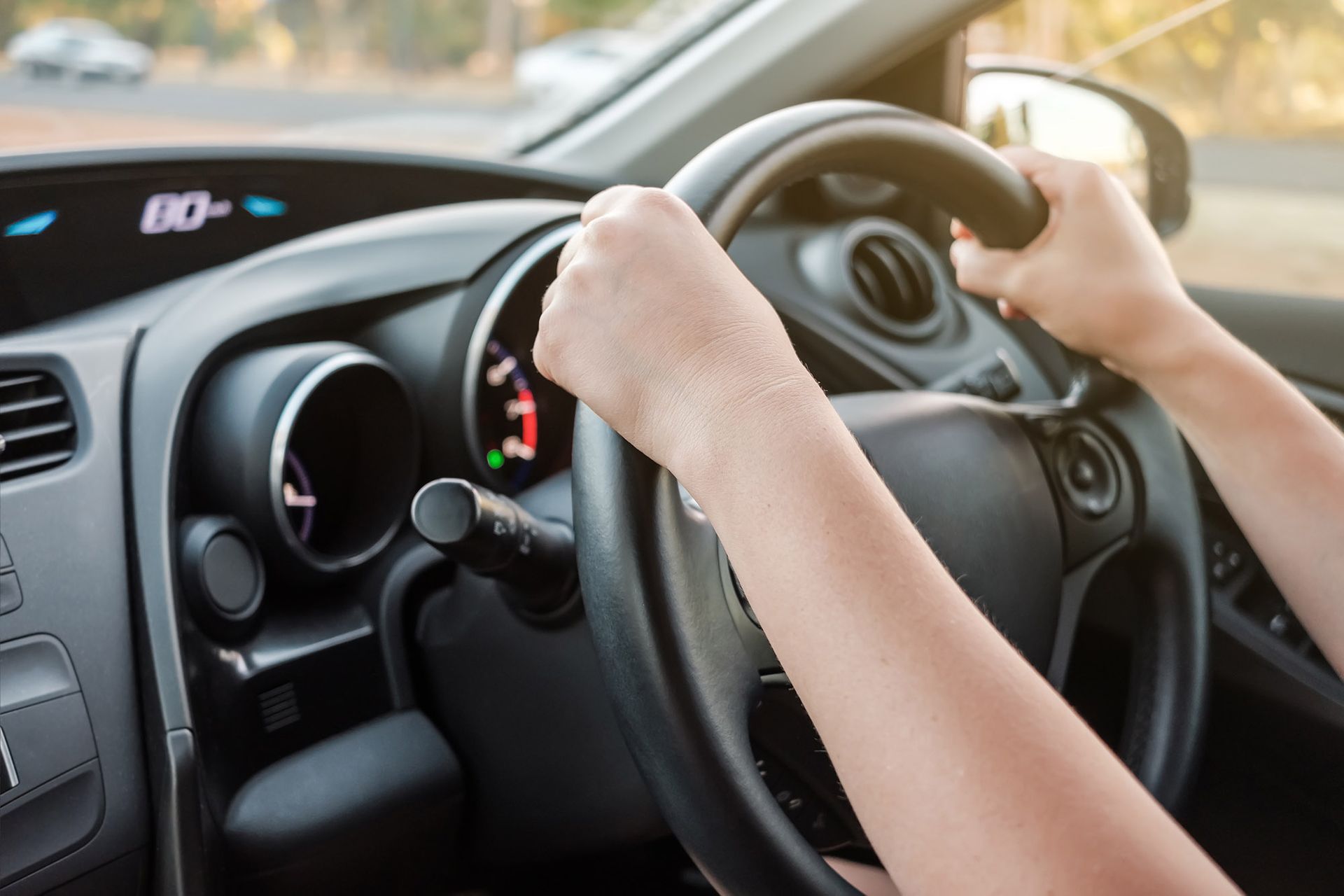 Hands gripping steering wheel in a car, dashboard visible.