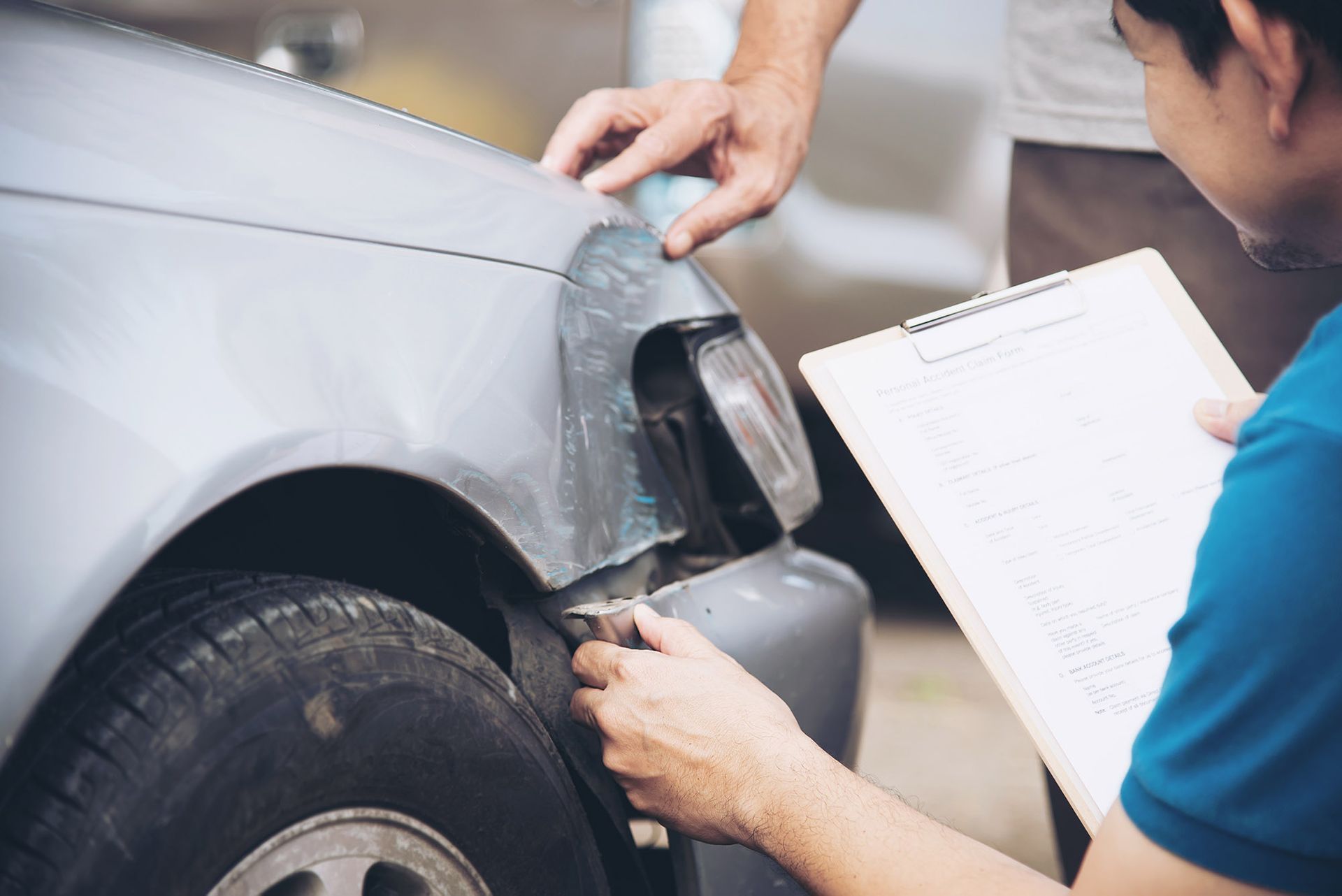 Two people examining a damaged car fender and headlight, one holding a clipboard.
