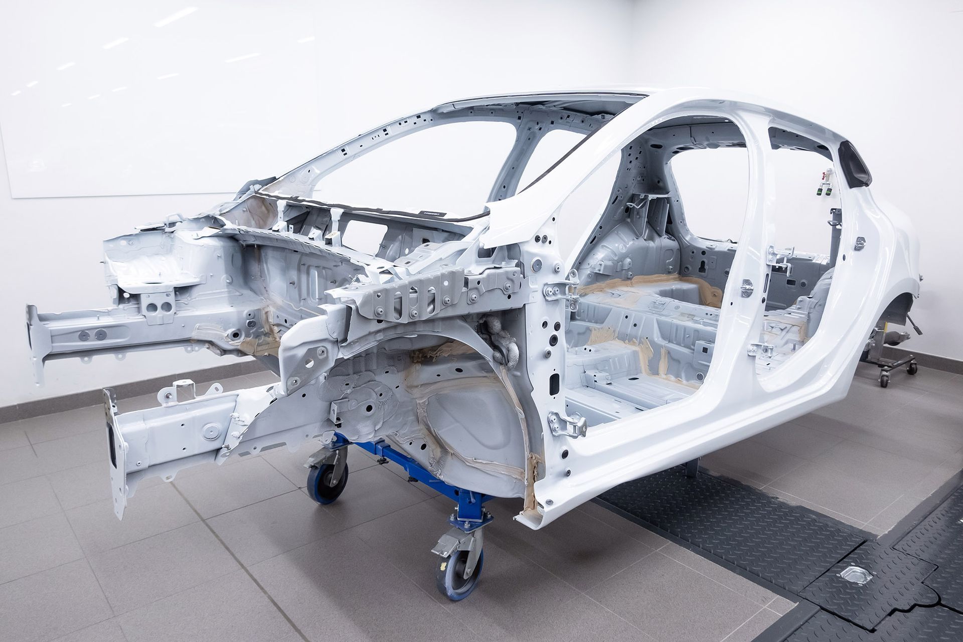 White car frame on wheels in a bright room.