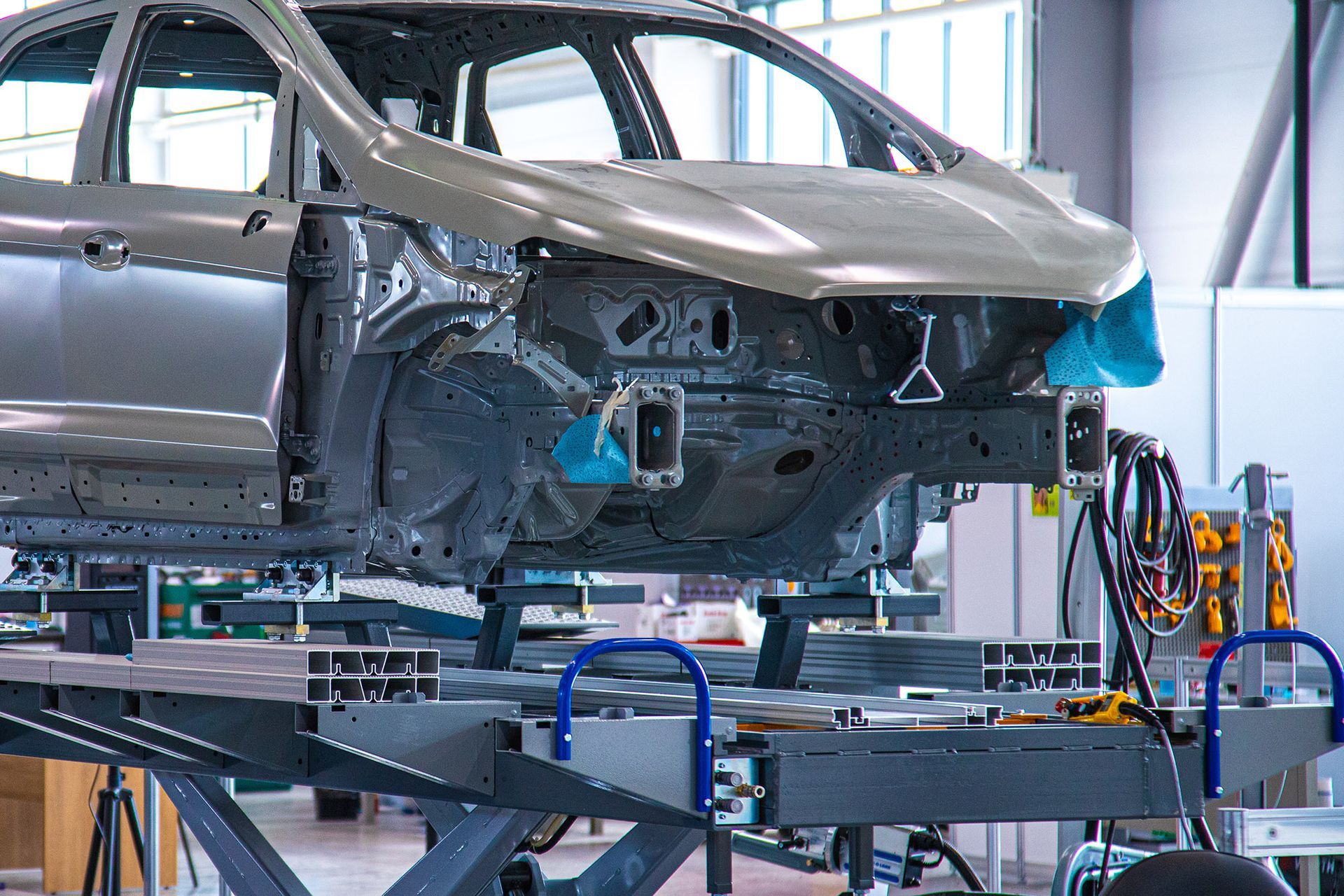 Car chassis on an assembly line. Grey metal, blue protective covering, industrial setting.