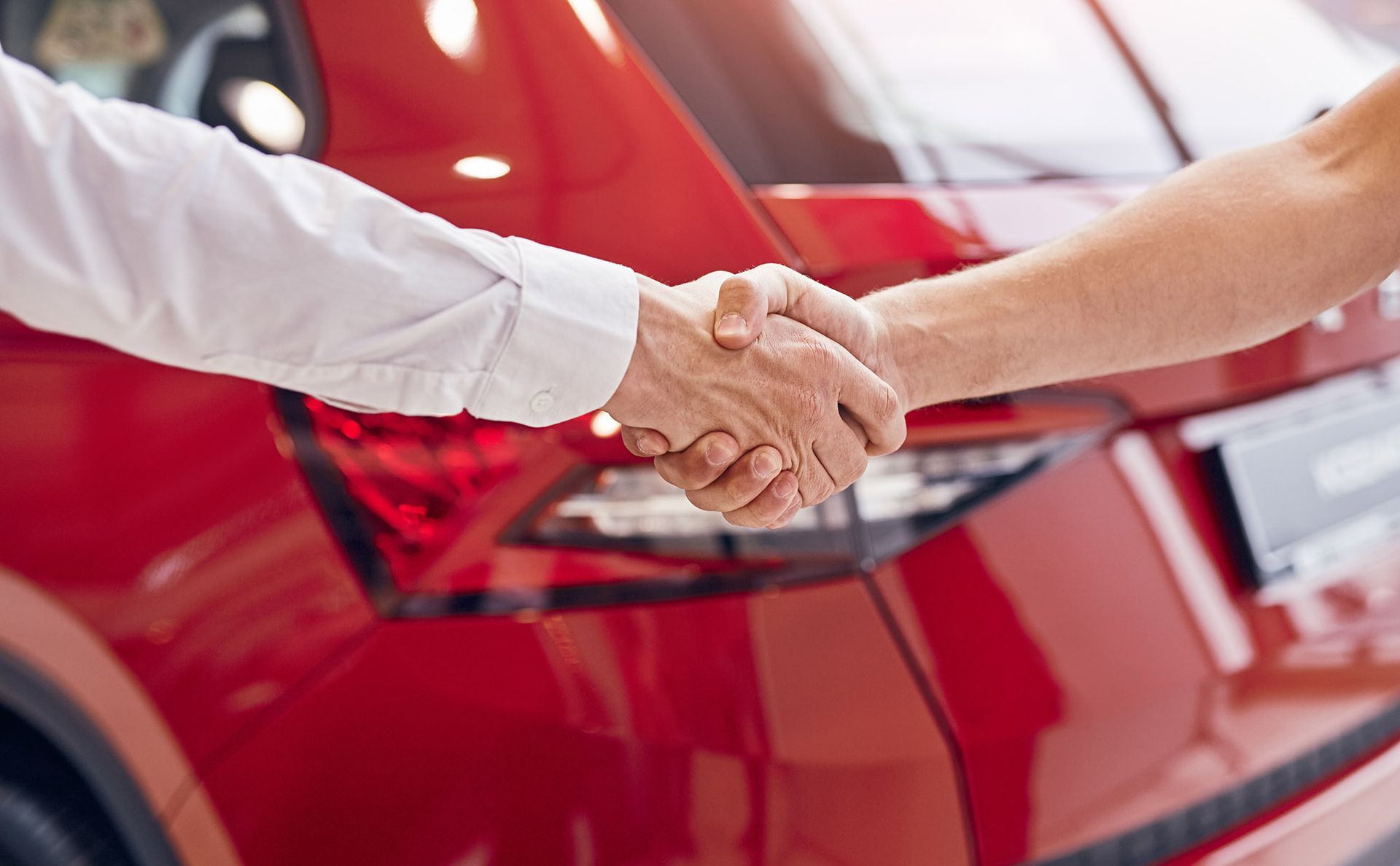 Hands shaking in front of a red car, possibly a car deal.