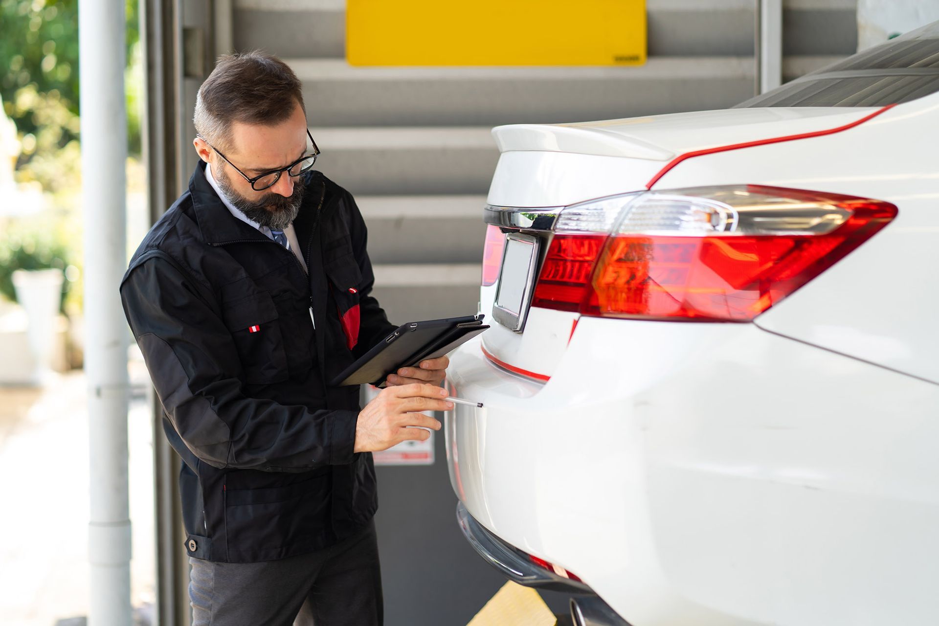 Mechanic inspecting a white car, using a tablet, in a garage.