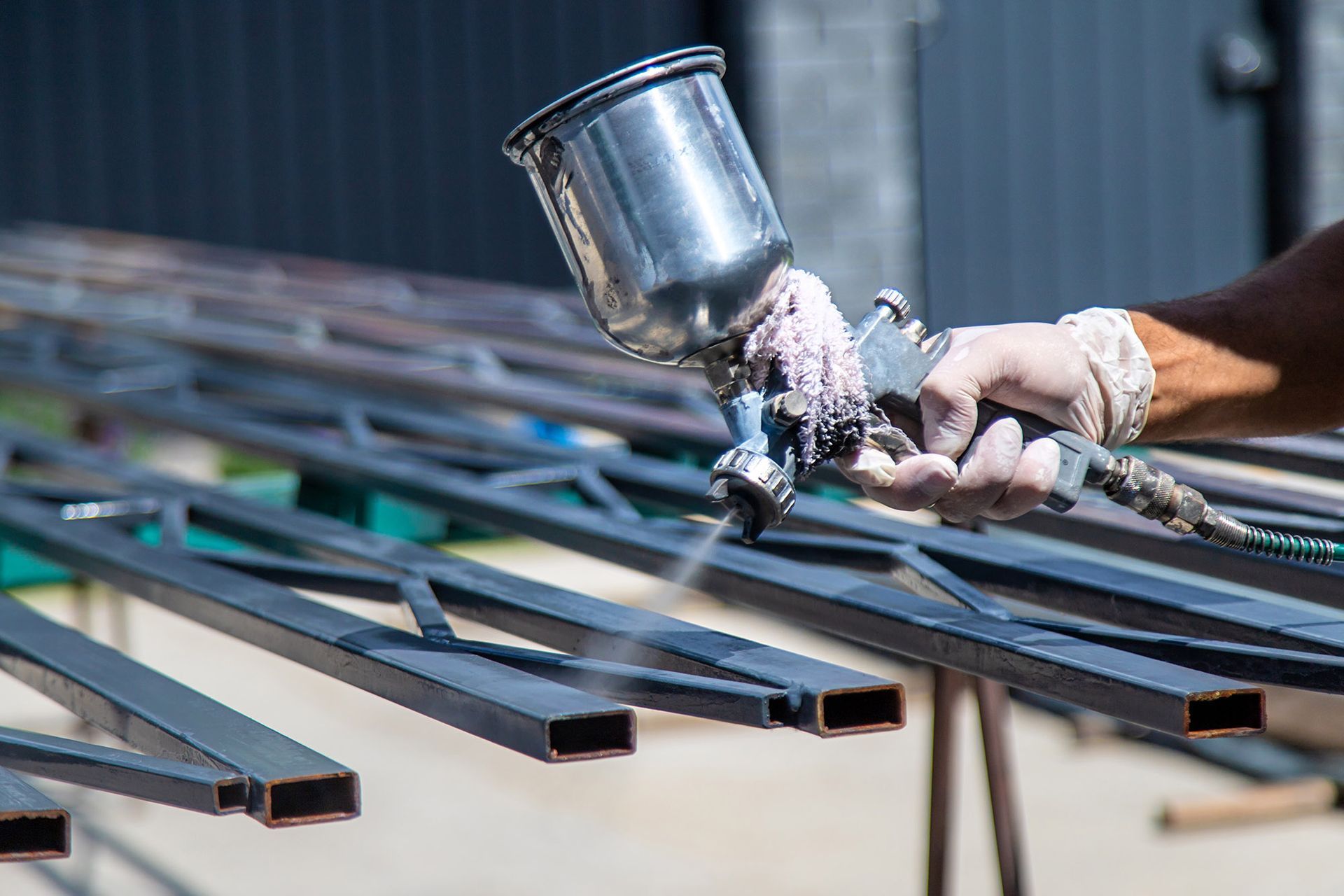 Person spray painting metal railings with a spray gun, outdoors.