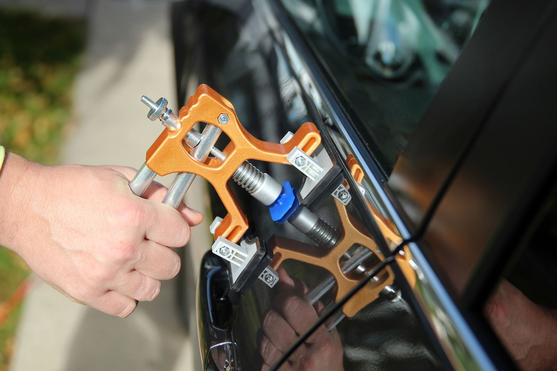 A person using a dent repair tool on a black car door.