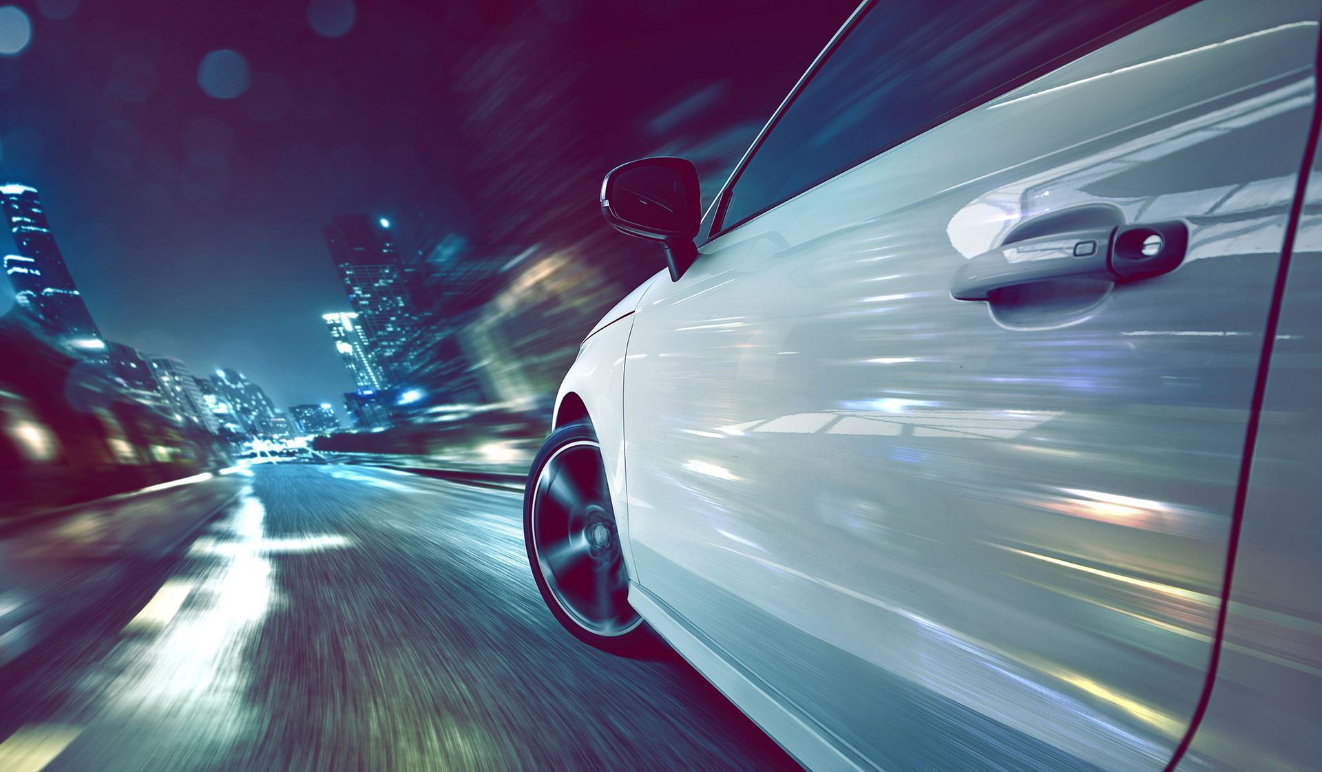 White car speeding down a city street at night with motion blur.
