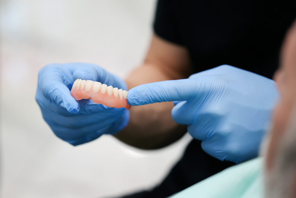 Dentist wearing blue gloves points to a set of upper dentures.