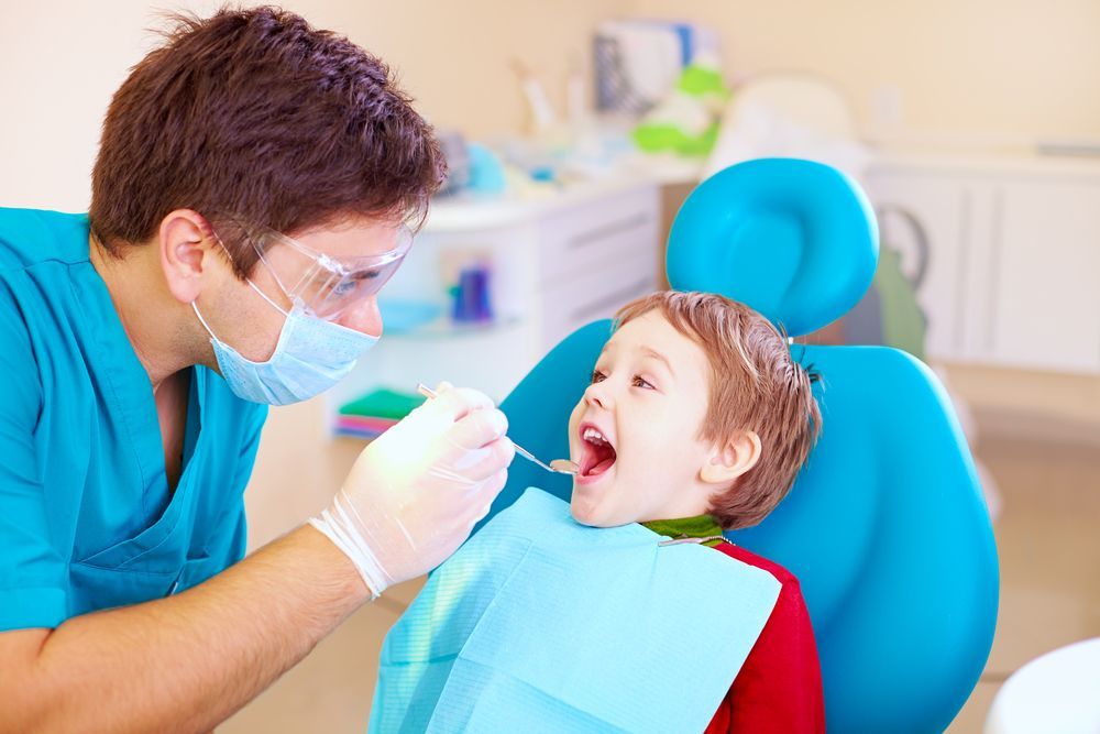 Dentist examining a young boy's teeth in a dental chair. Boy is opening his mouth.