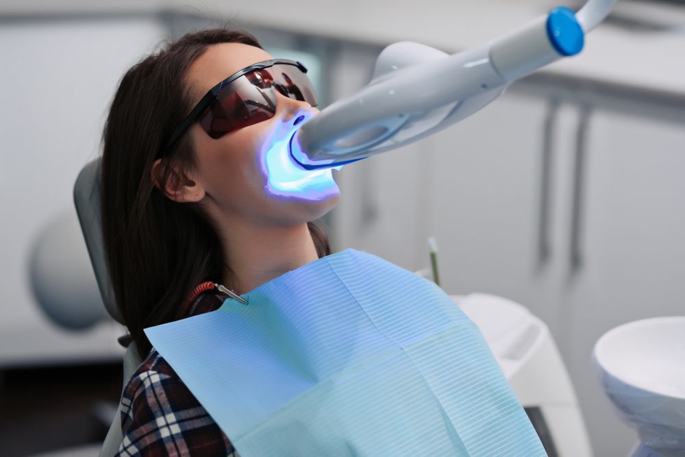 Woman getting teeth whitened with blue light at a dental clinic.