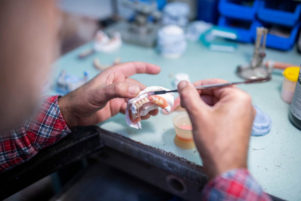 Person in plaid shirt working on dentures in a dental lab, using a brush and tools.