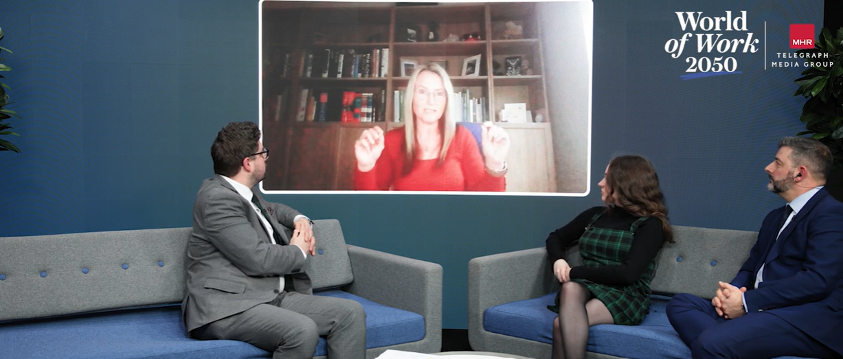 Three people on a couch watching a Zena on a screen. The Zena is in a red shirt. The wall is blue.