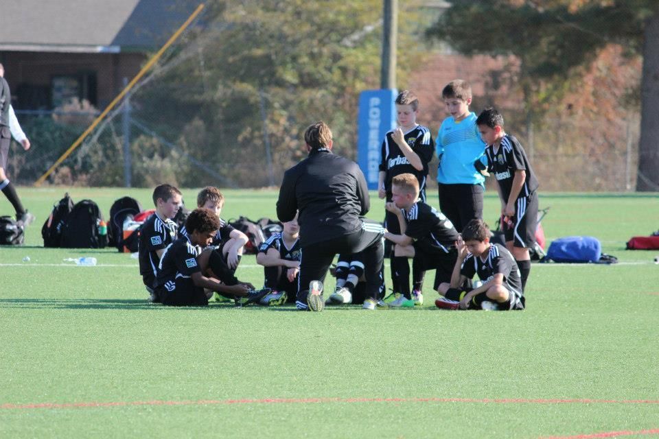 Team Challenger FC team huddles on a field with a coach