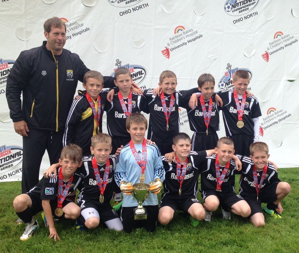 Team Challenger FC team with coach posing with medals and a trophy on a field