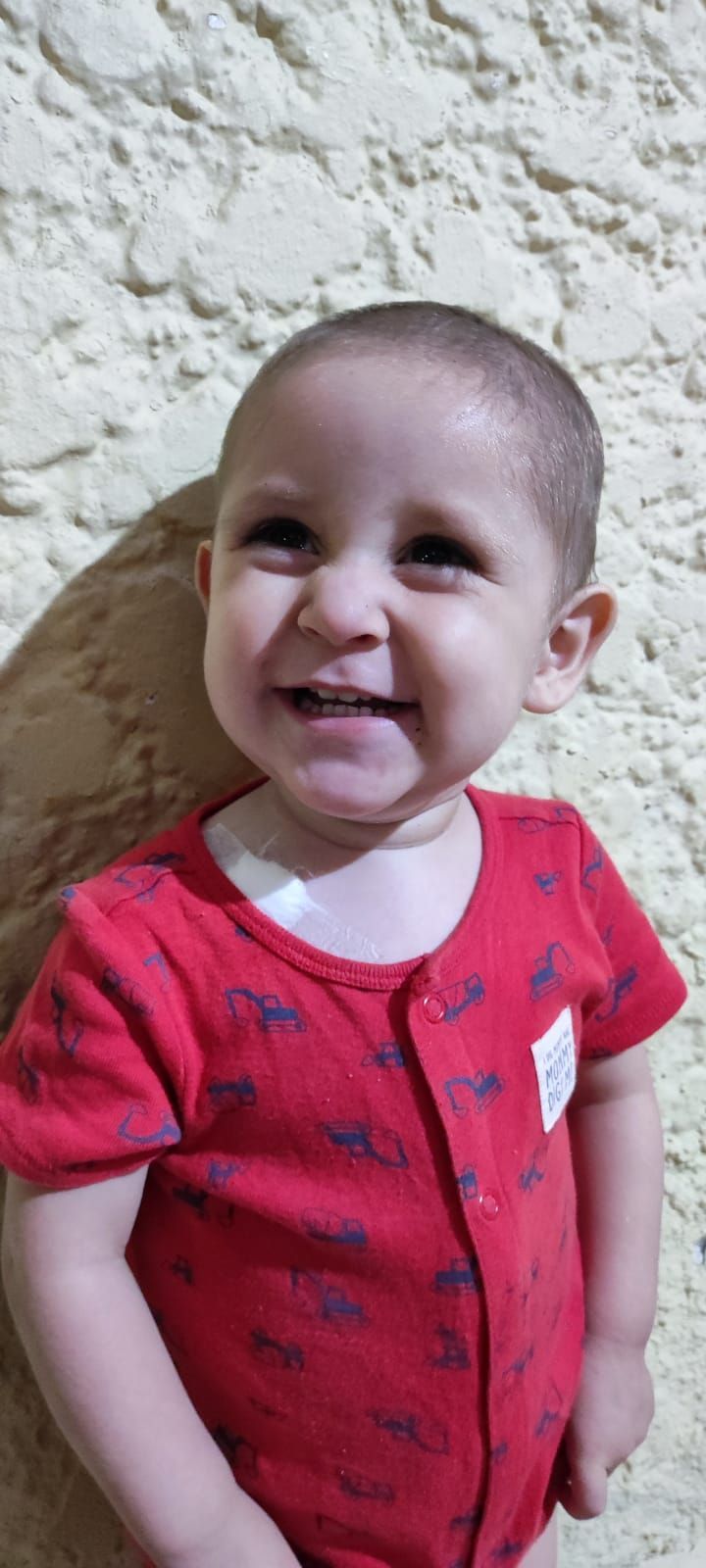 Niño sonriente vistiendo un mono rojo frente a una pared beige texturizada.