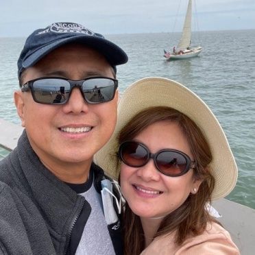 A man and woman are posing for a picture with a sailboat in the background