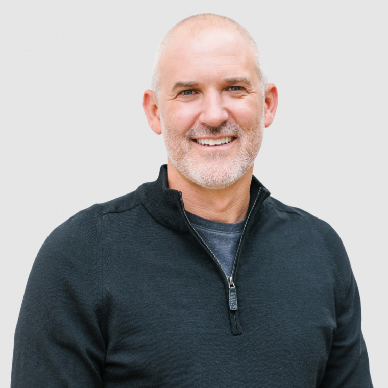 A man with a beard is wearing a black sweater and smiling.