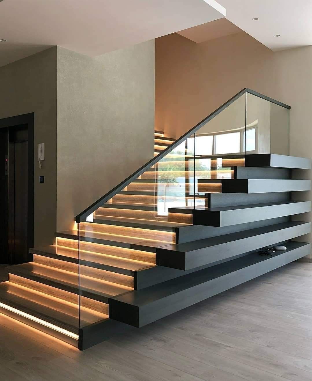 Modern indoor staircase with glowing step lights, dark treads, and glass railing in a contemporary home interior