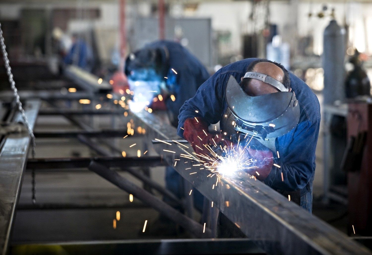 Workers welding metal in a factory, with bright sparks and blue protective gear
