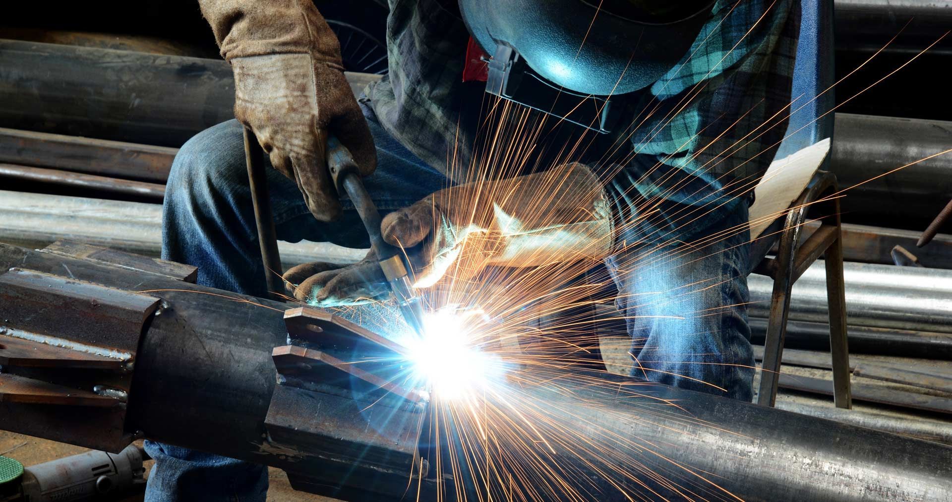 Worker welding metal pipe with bright sparks in an industrial setting