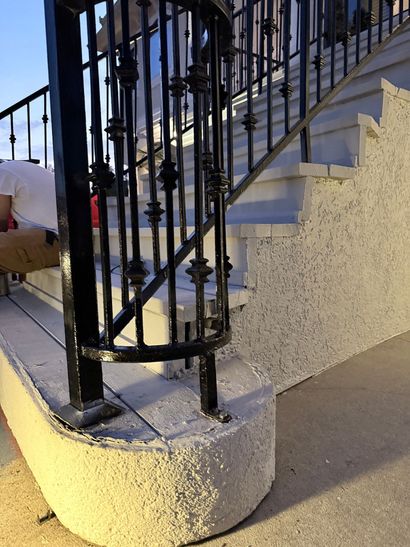 Black metal spiral staircase on a white concrete base outdoors at dusk