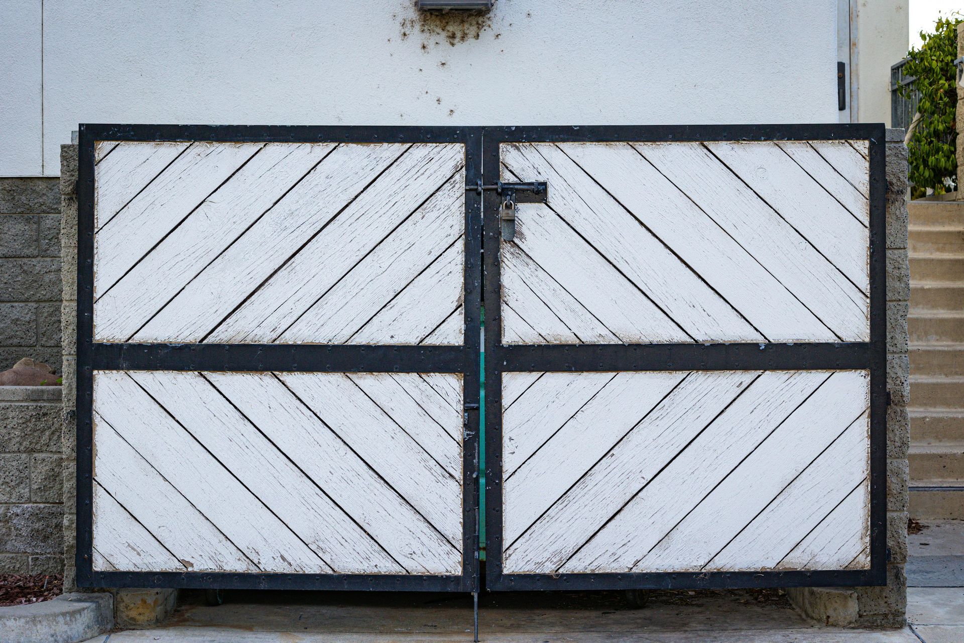 White wooden double gate with diagonal slats and black metal frame in front of a wall