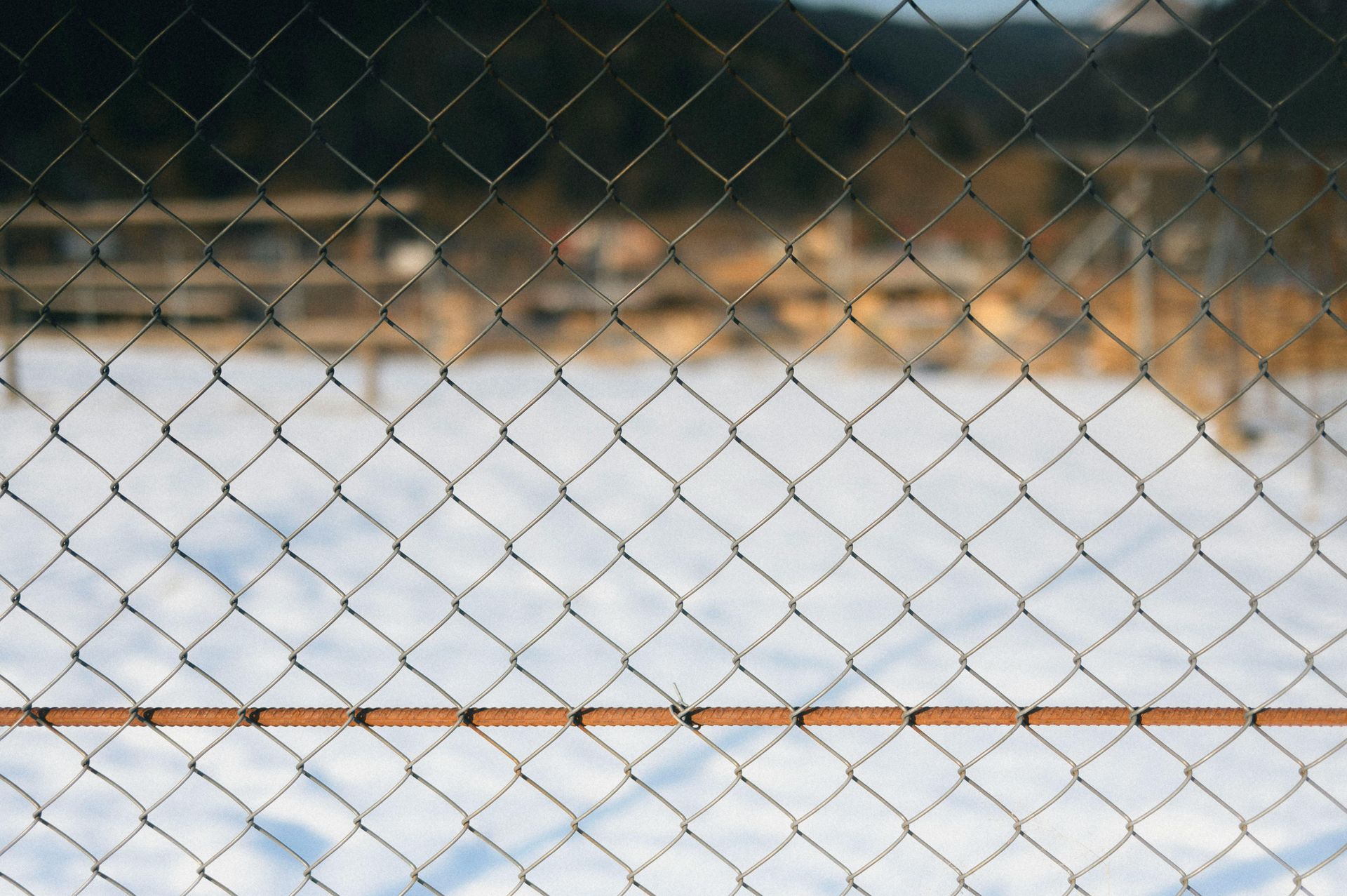 Chain-link fence in front of a snowy field with blurred mountains in the background