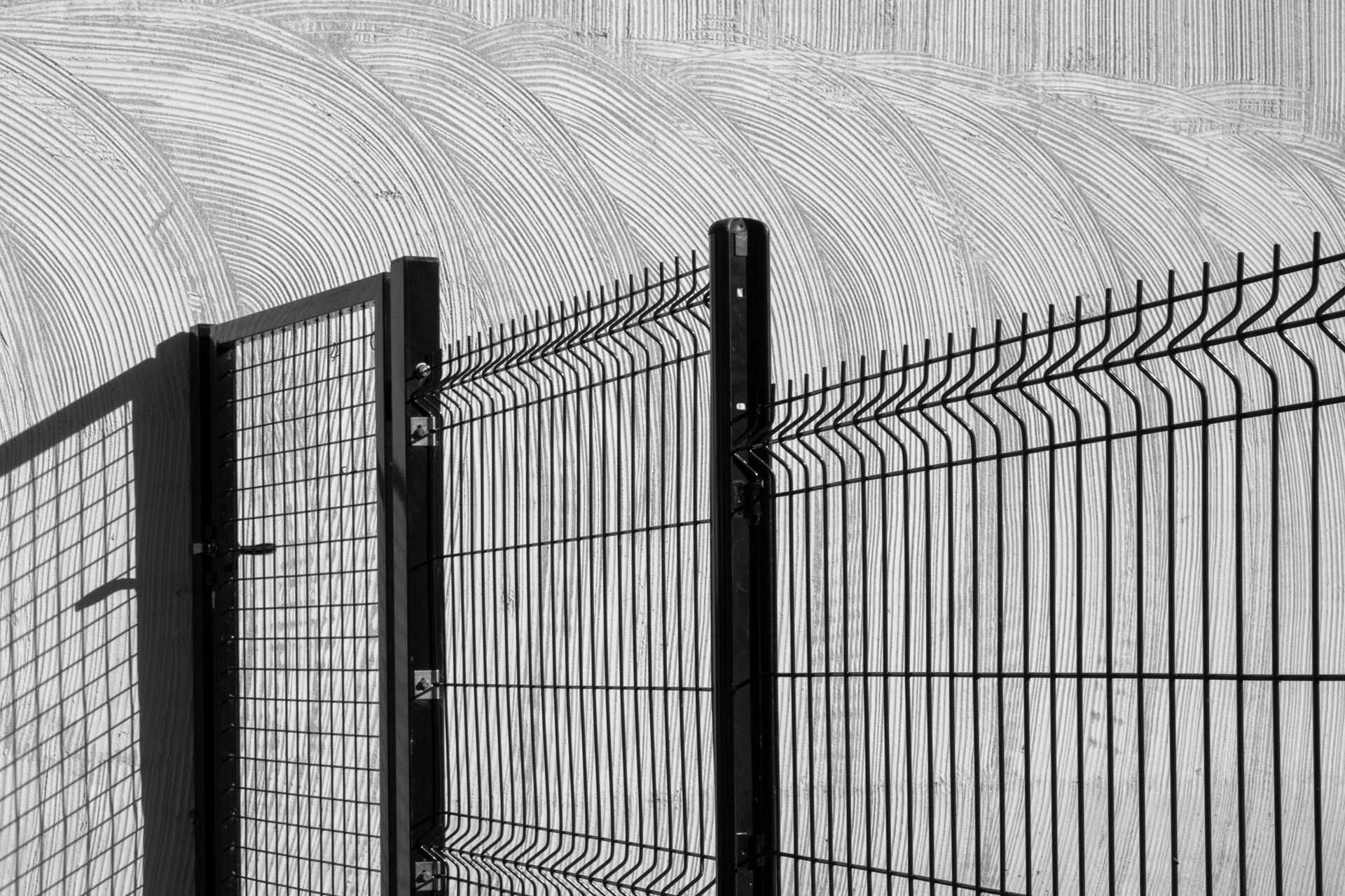 Black metal fence topped with barbed wire against a gray concrete wall