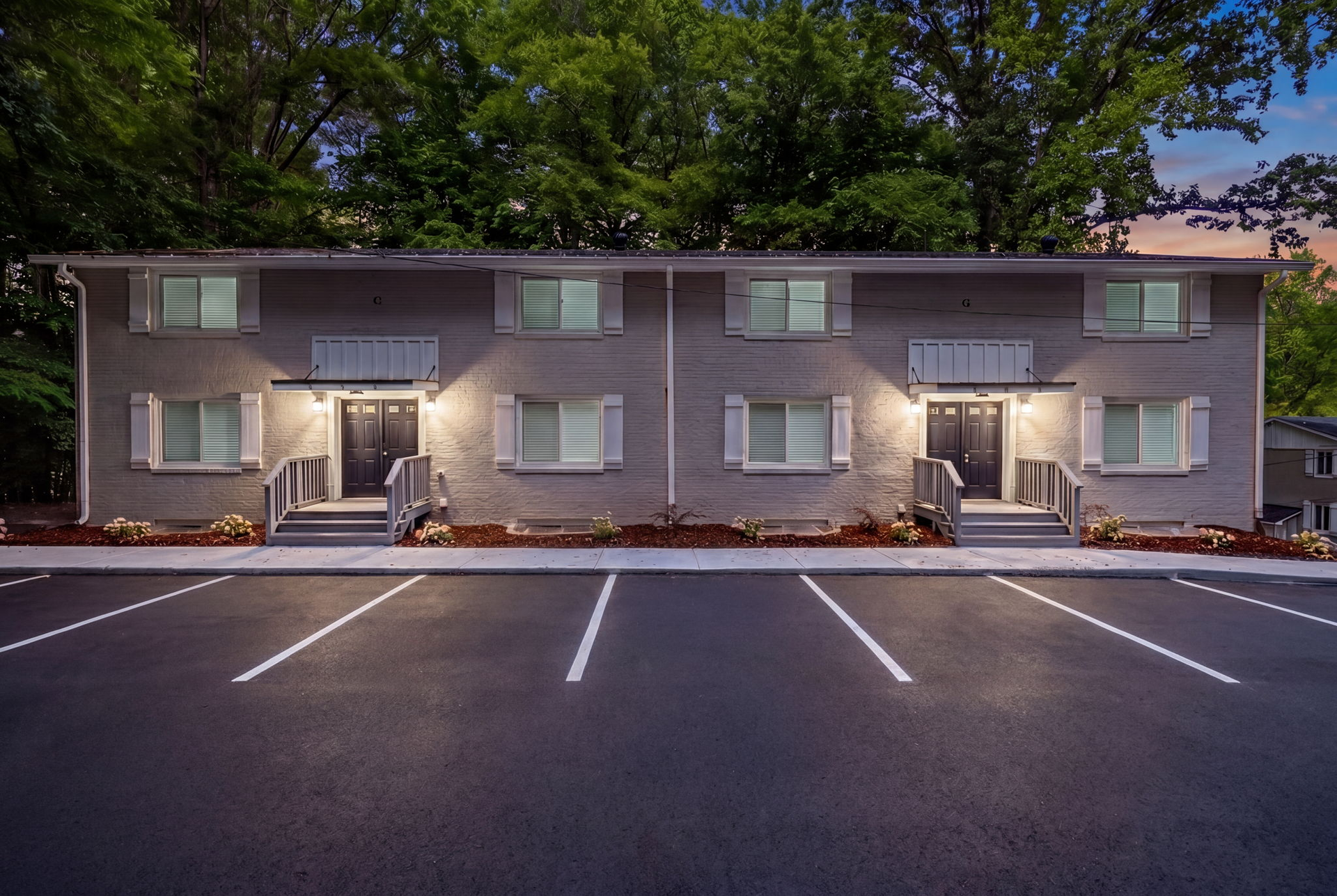 Apartment building at dusk with lit entrances and empty parking spaces in front