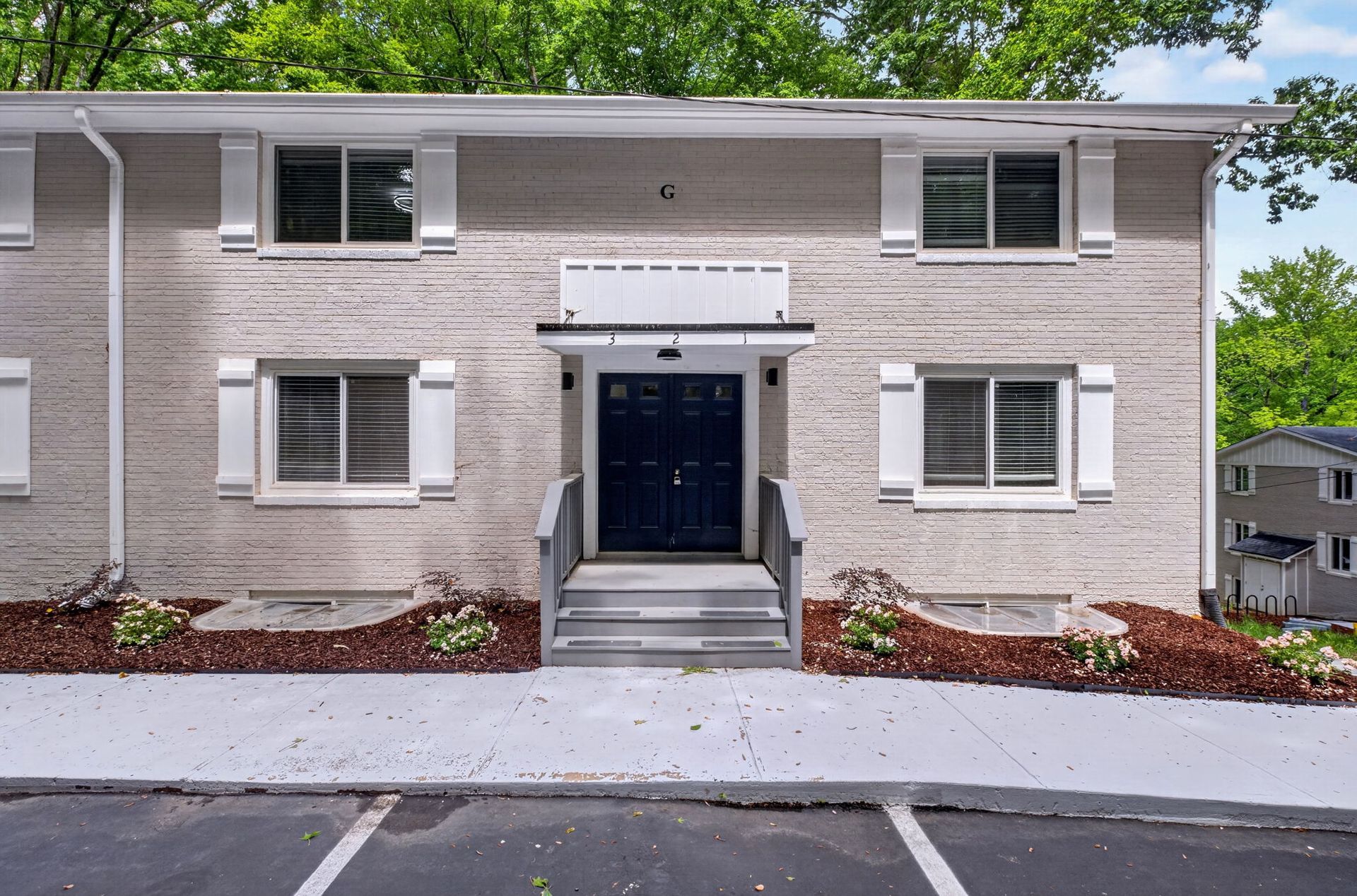 Front view of a light brick apartment building with a central entrance and parking spaces in front