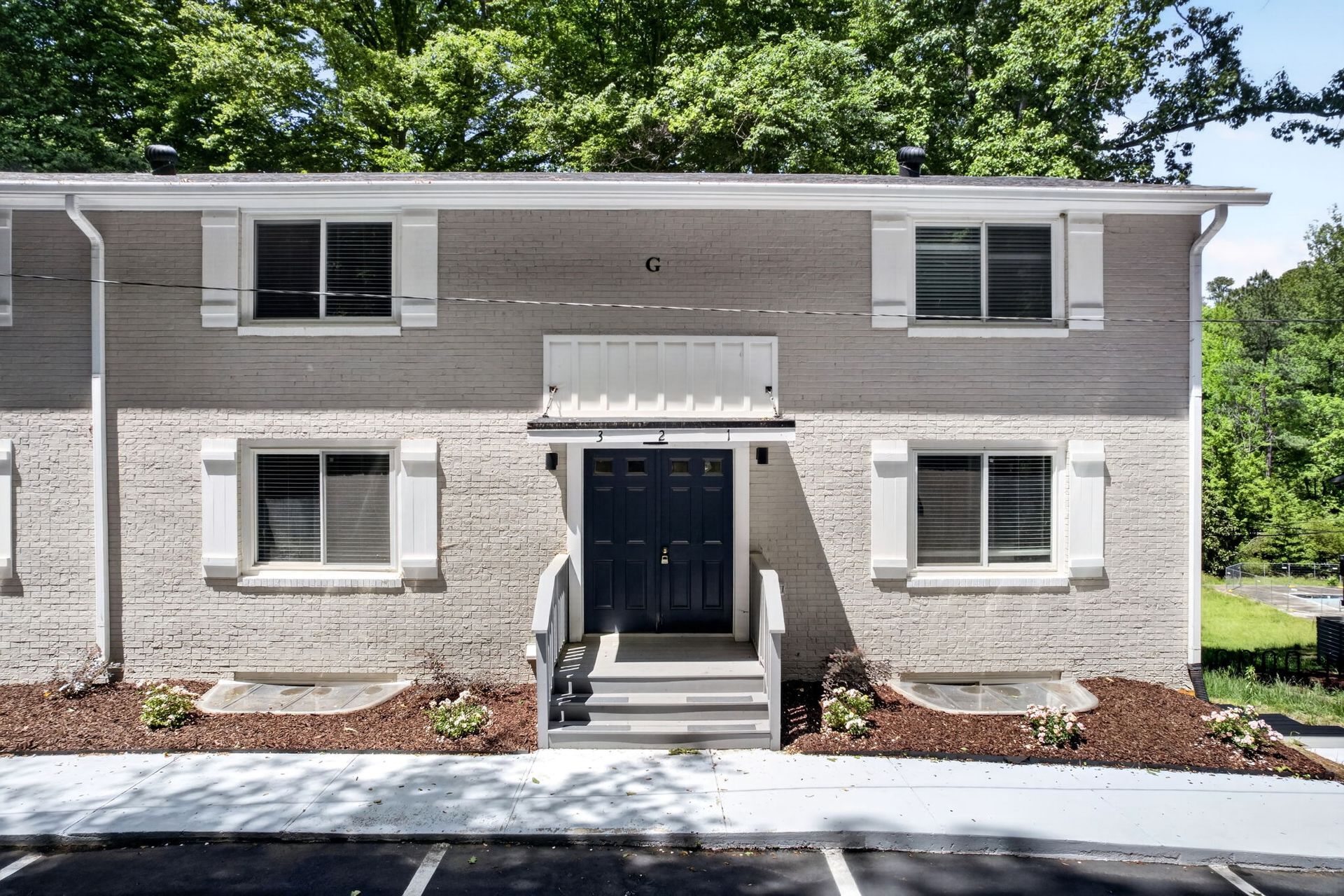 Front view of a gray two-story apartment building with black door, white trim, and landscaped entrance