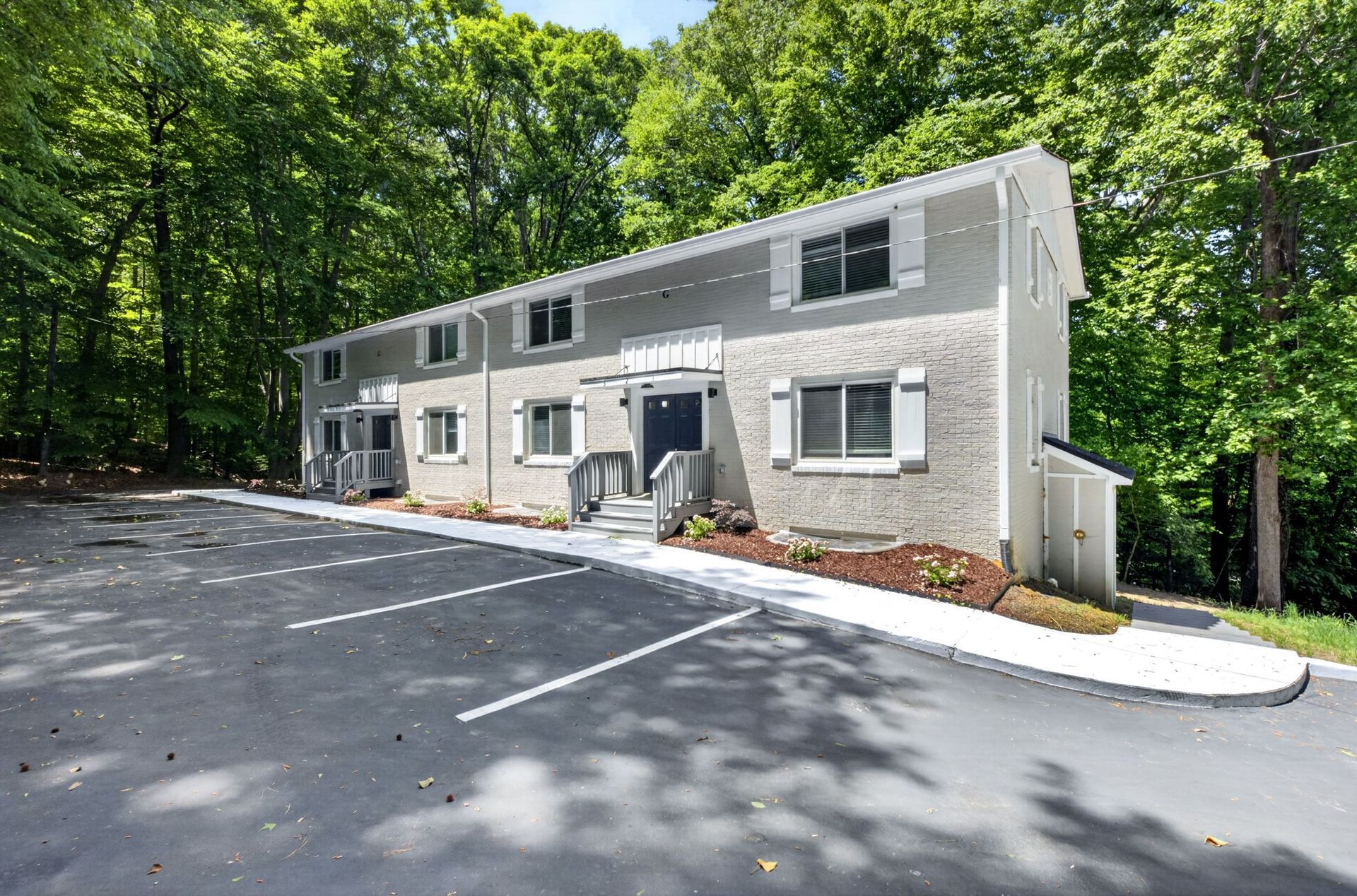Two-story gray apartment building with parking lot and trees in front