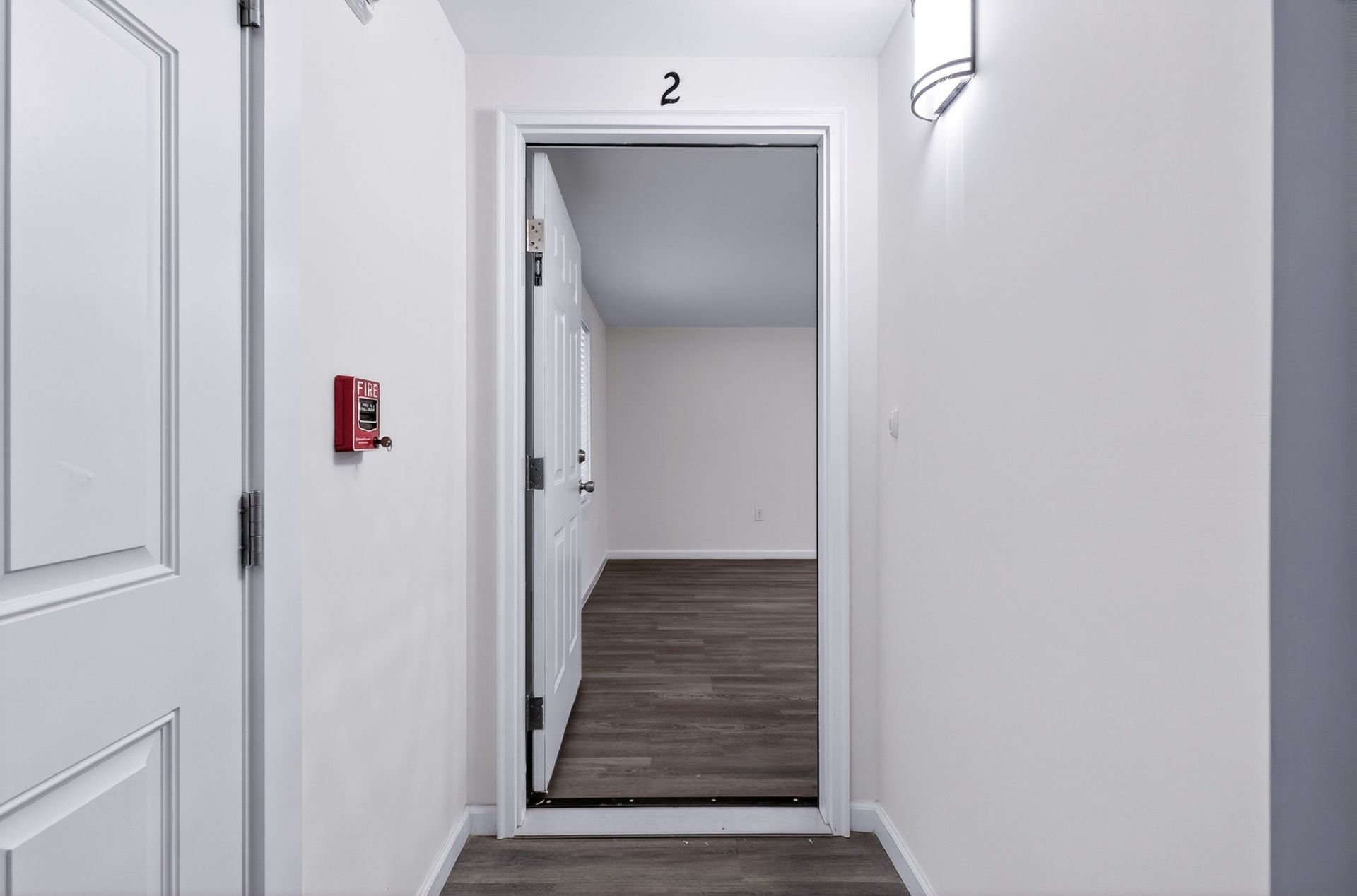 White apartment hallway with an open door labeled 2 and dark flooring beyond