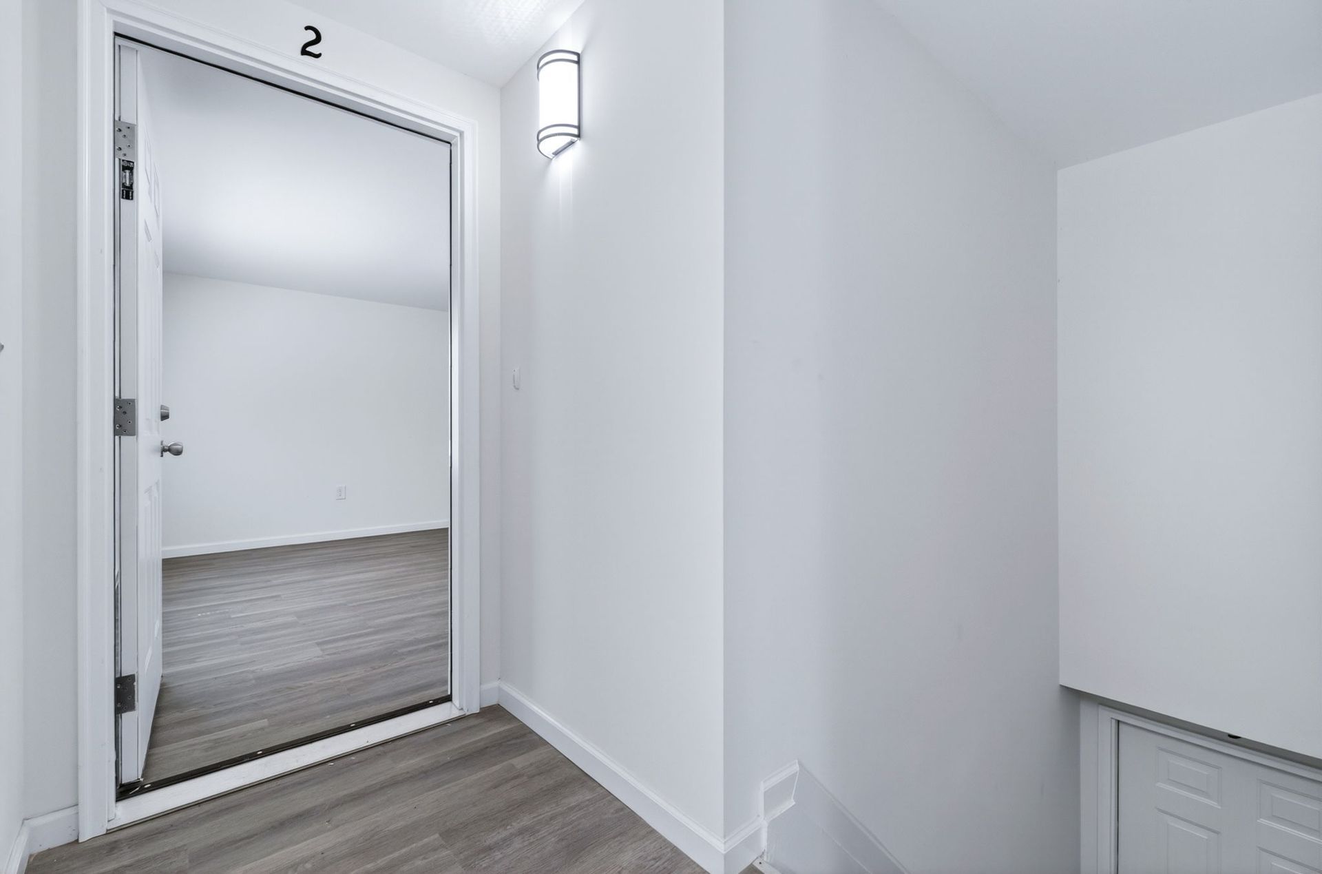 Empty white hallway with an open doorway and gray wood-look flooring