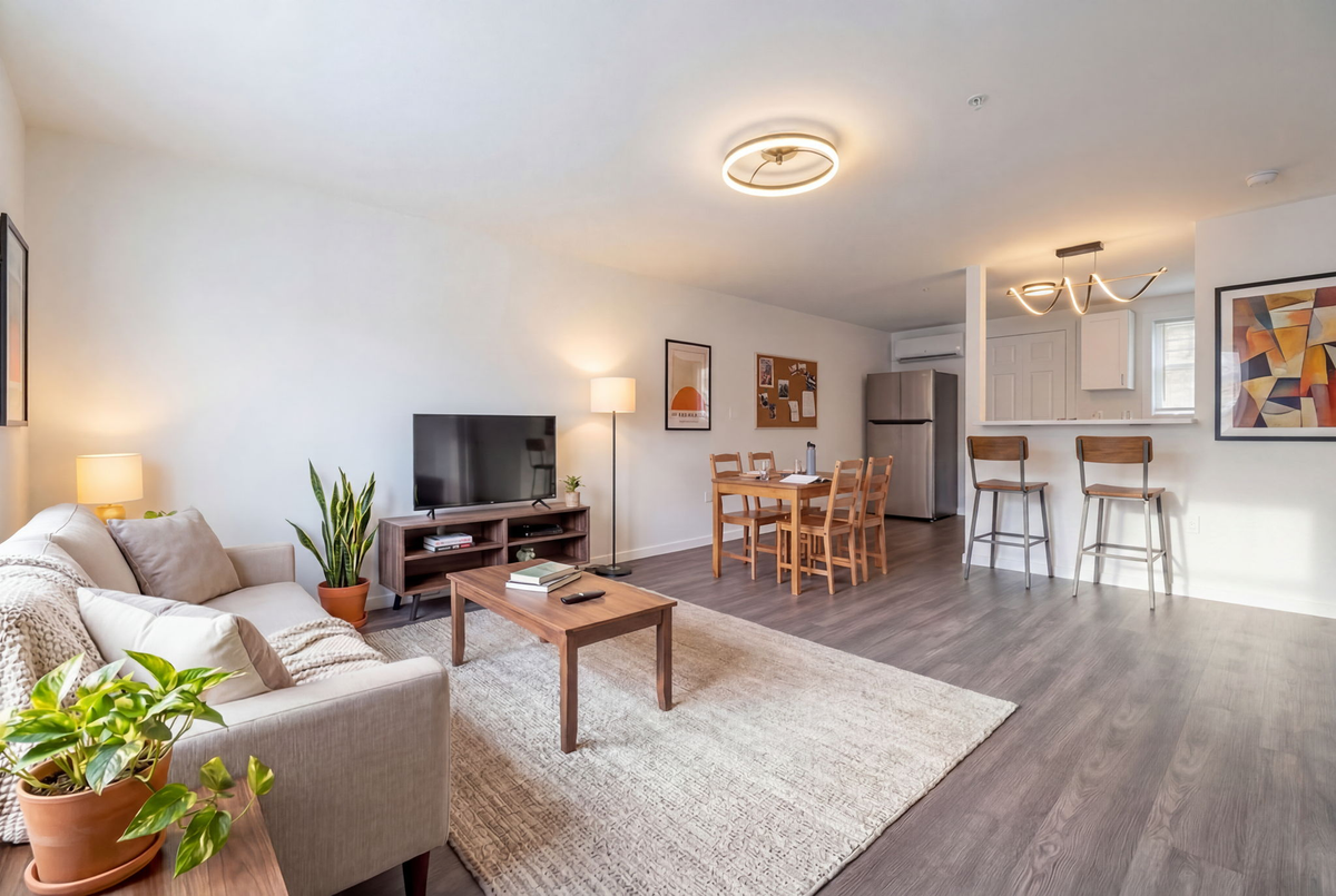 Bright modern living room with gray sofa, TV, coffee table, dining area, and open kitchen.