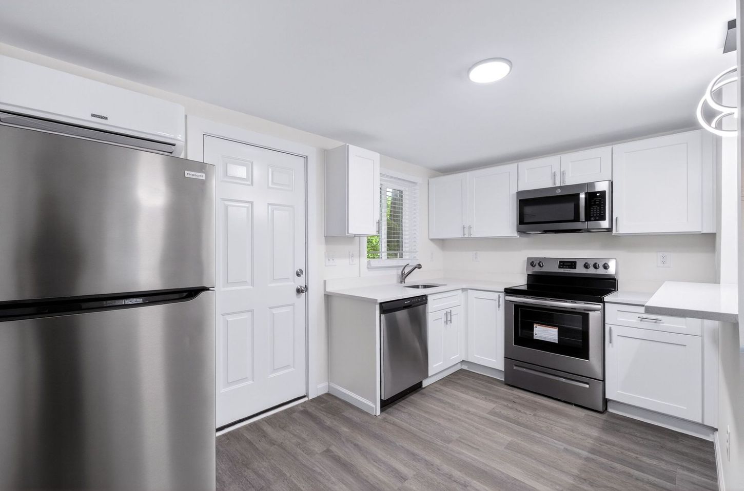 Modern white kitchen with stainless steel appliances, gray flooring, and bright overhead lighting
