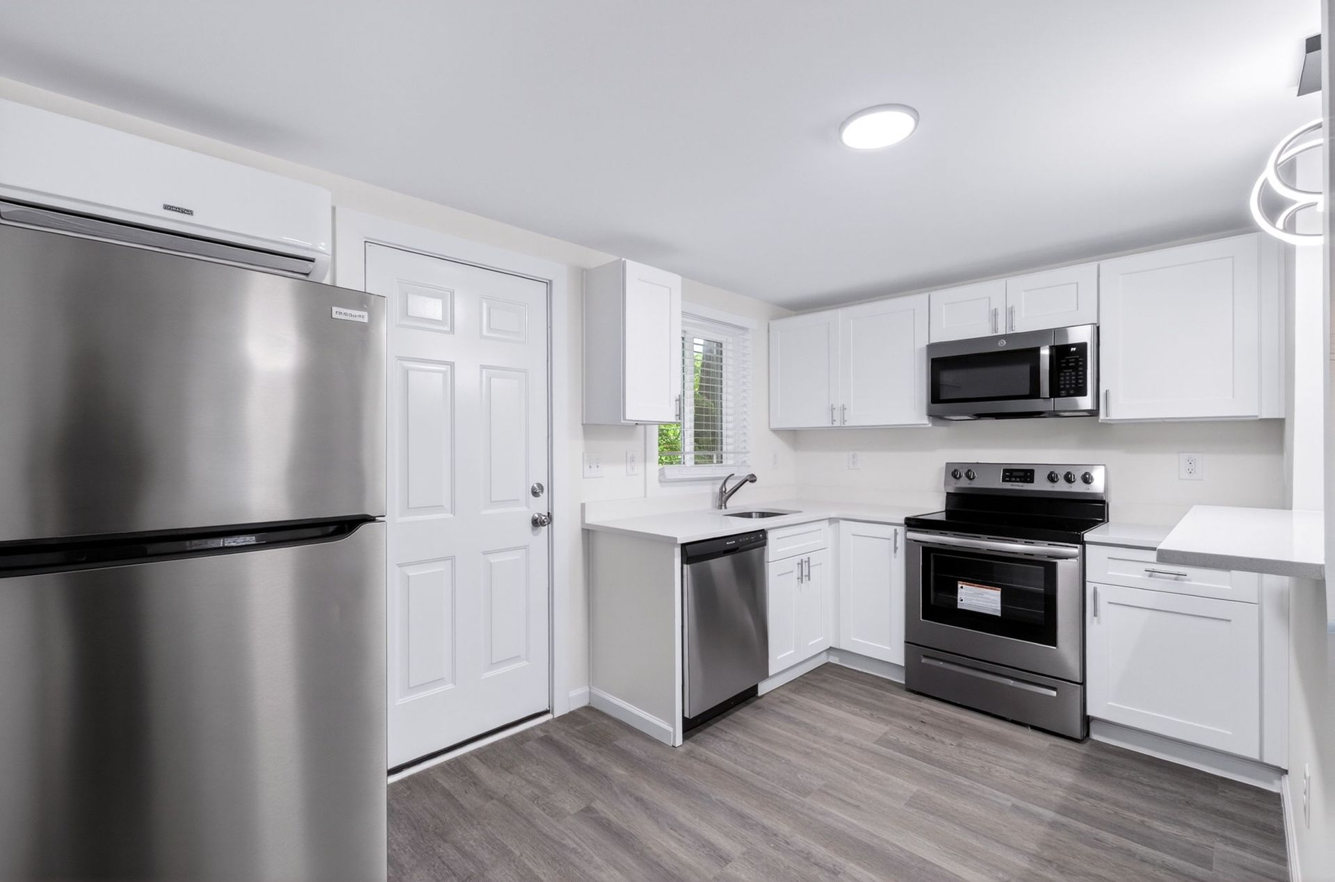 Modern white kitchen with stainless steel appliances, gray flooring, and bright overhead lighting