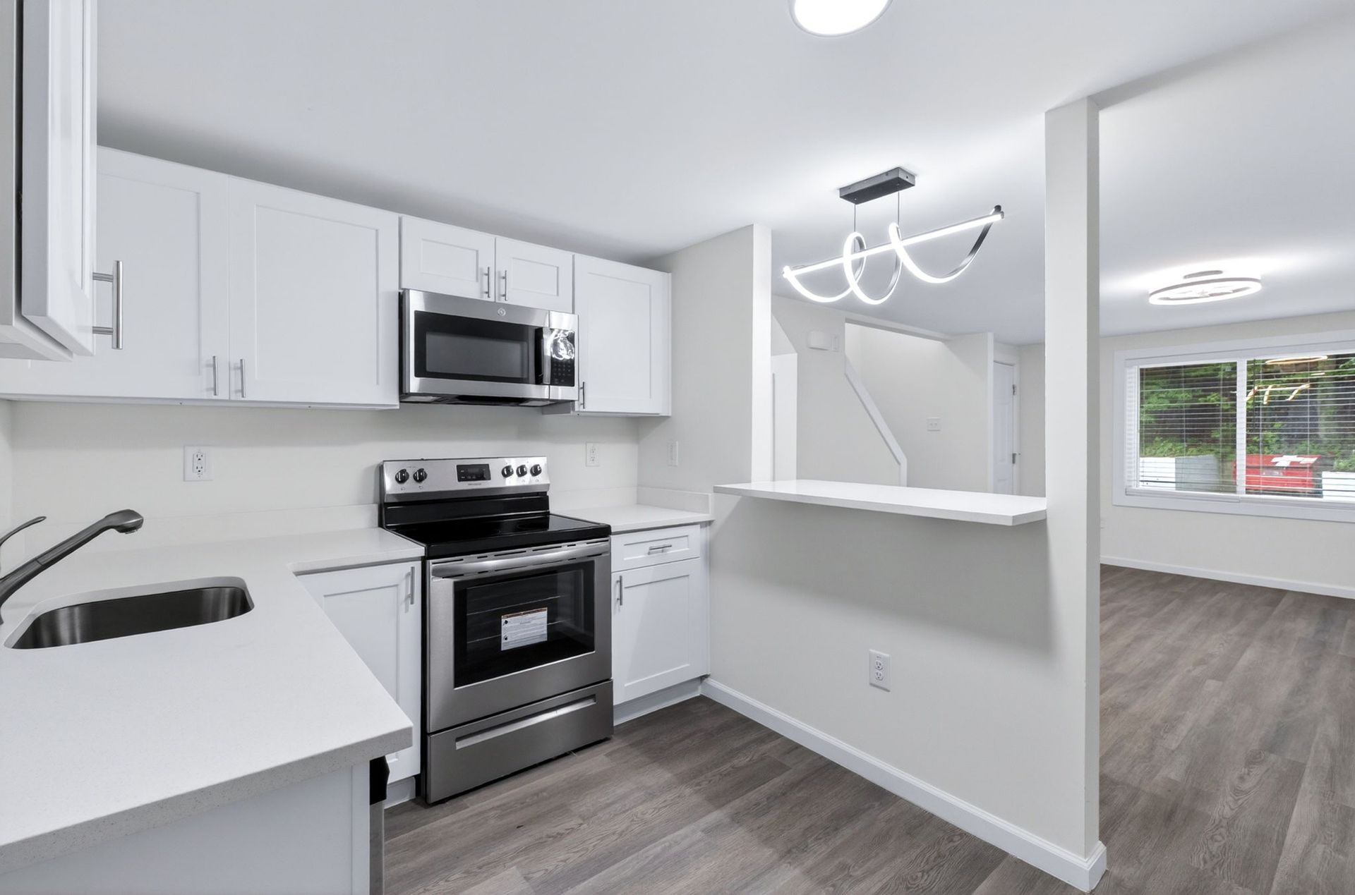 Bright modern kitchen with white cabinets, stainless steel appliances, and a breakfast bar opening to a hallway