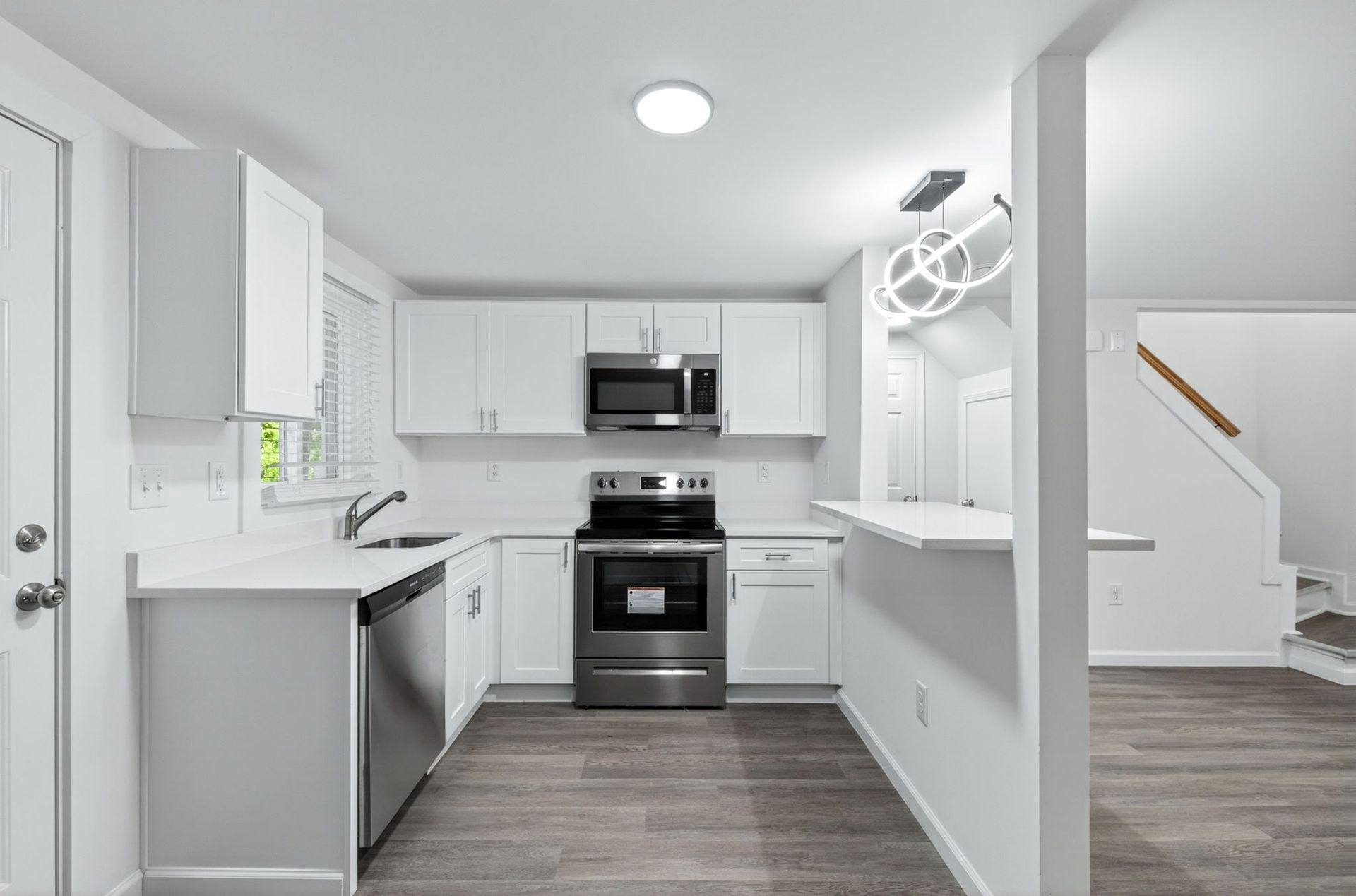 Bright white kitchen with stainless steel appliances, gray flooring, and a staircase visible to the right