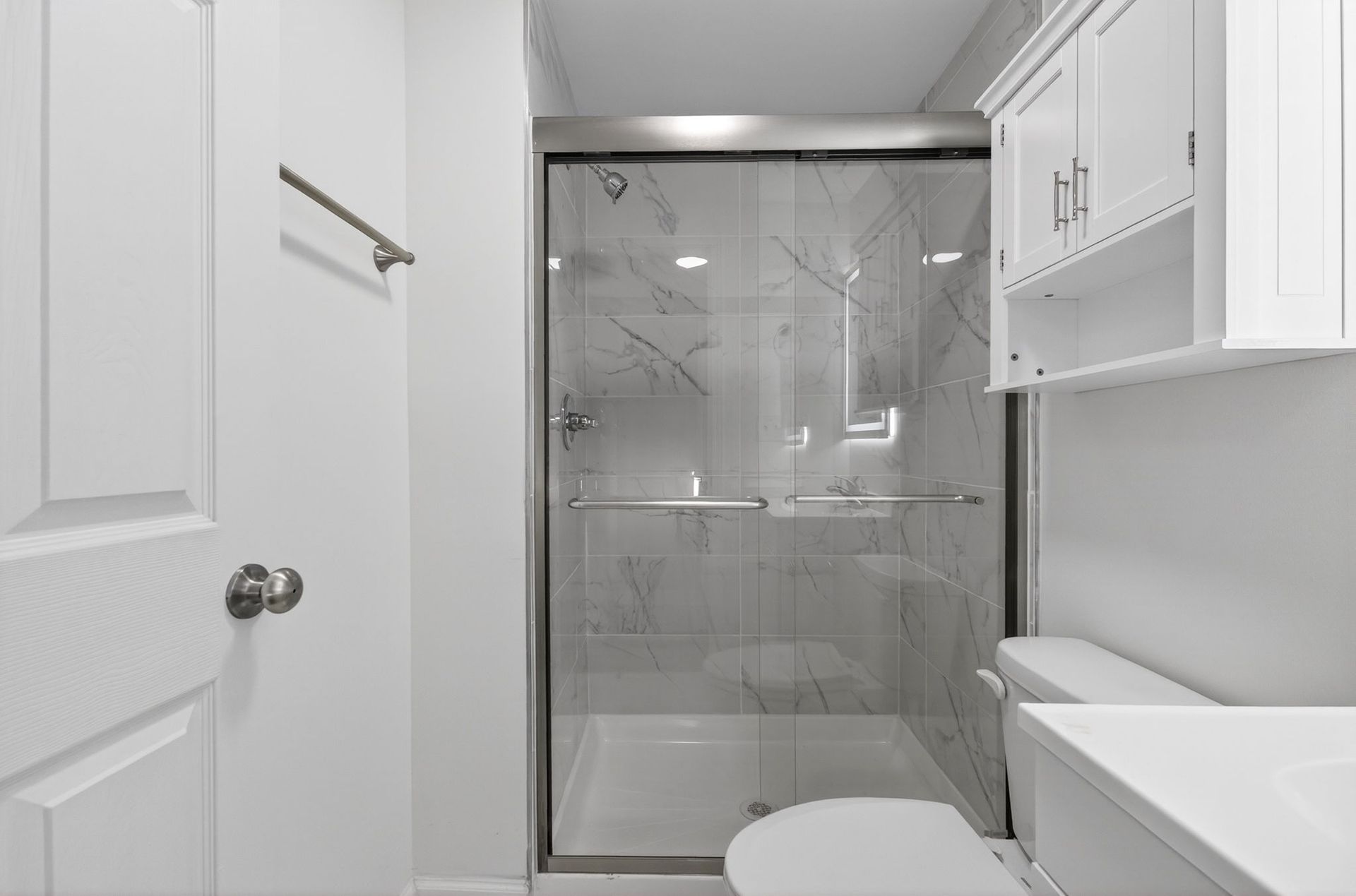 Bright white bathroom with glass-enclosed shower, vanity, and toilet.