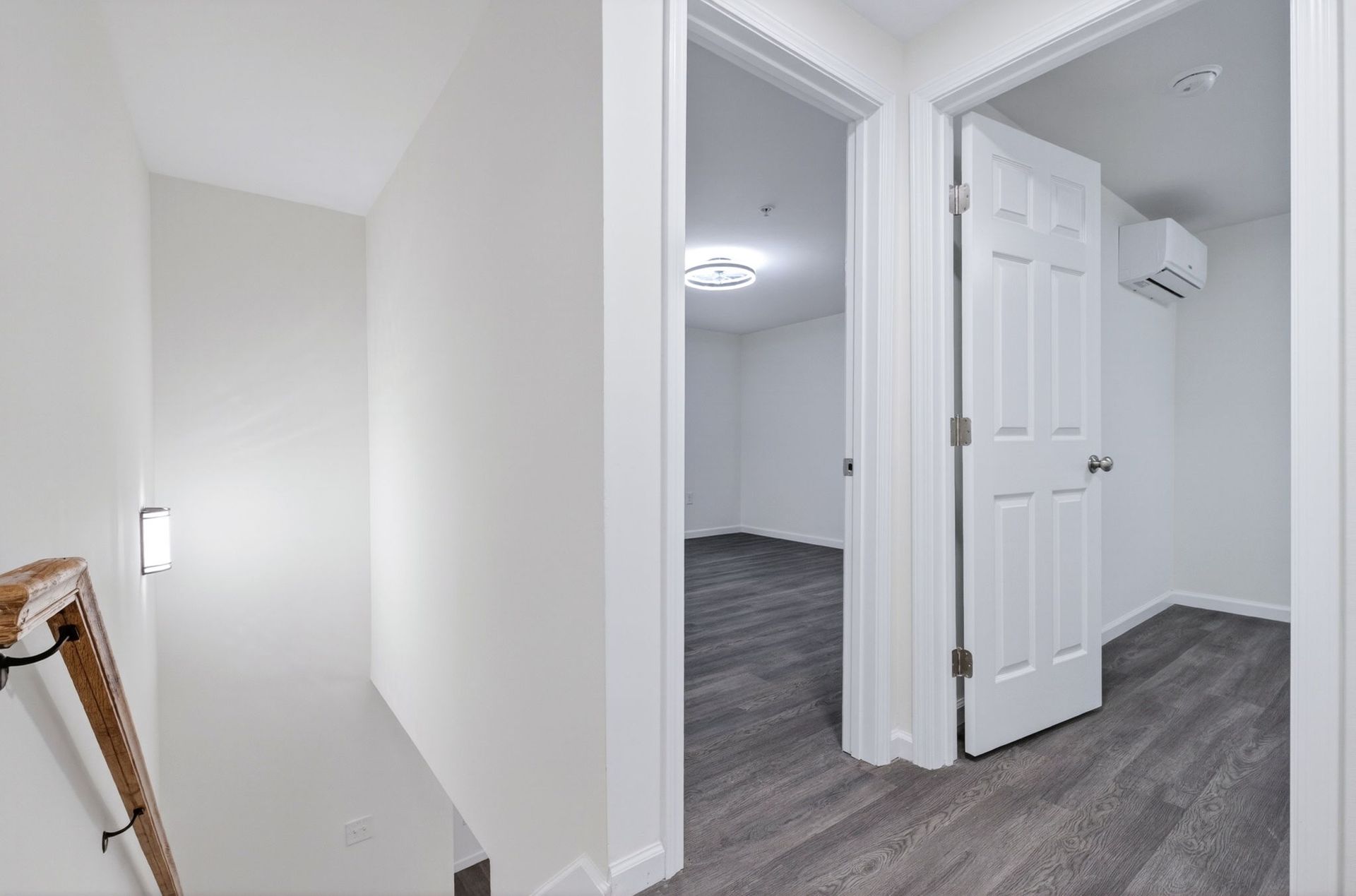 Bright hallway with white walls, gray carpet, open doors, and a staircase railing on the left