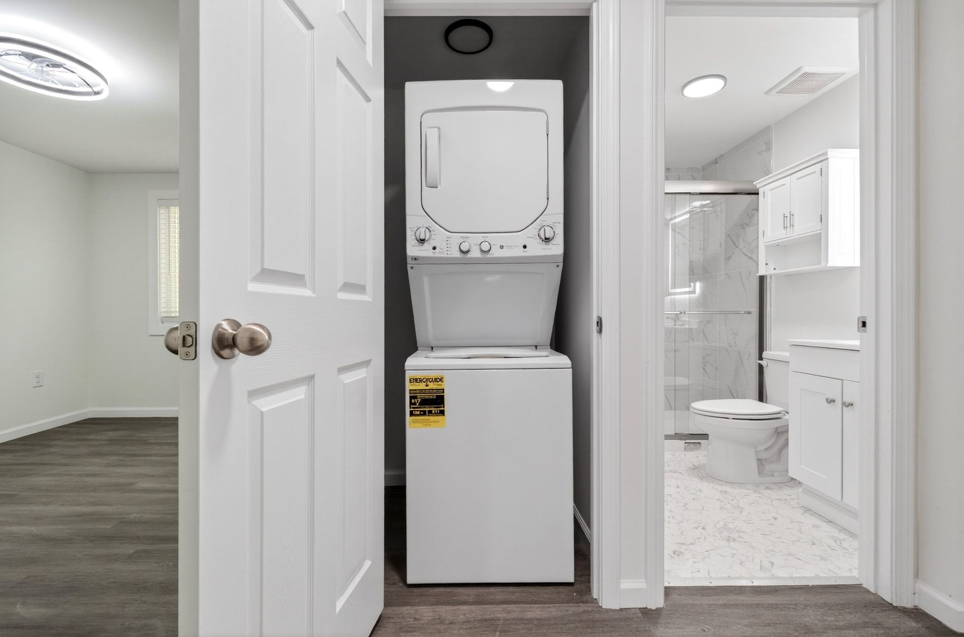Laundry closet with stacked washer and dryer beside a bathroom doorway and vanity sink