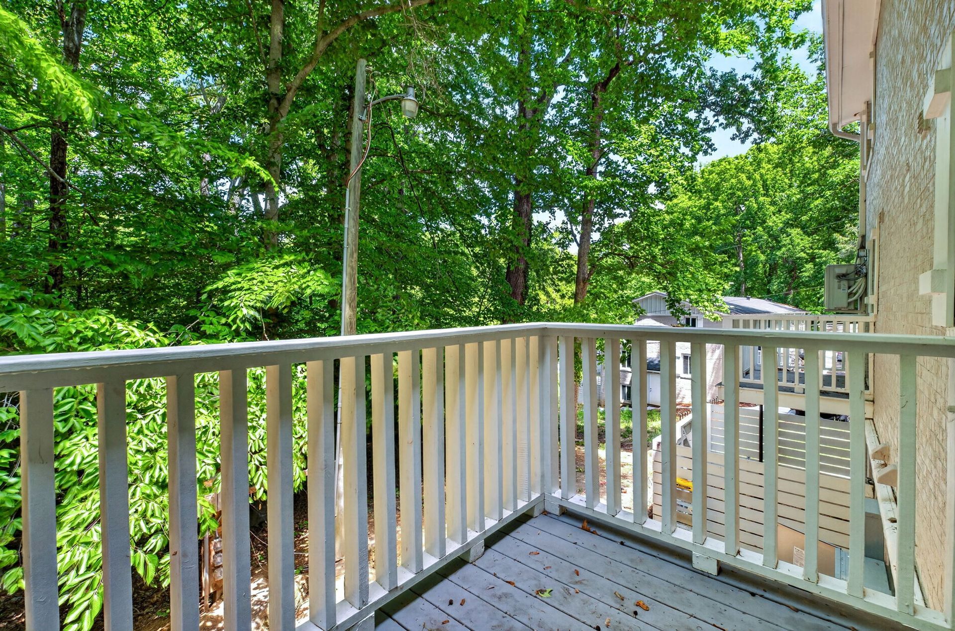 Wooden deck with white railing overlooking a lush green forest on a sunny day