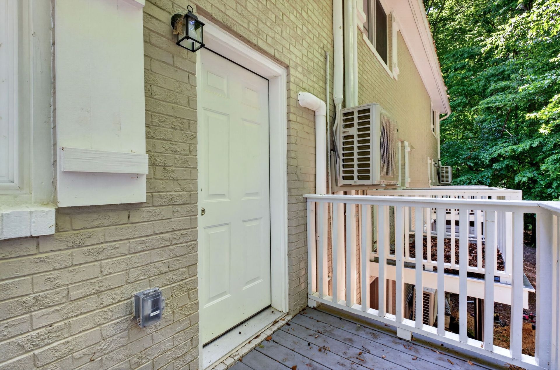 Exterior brick apartment entrance with white door, shutters, and a small deck with railing