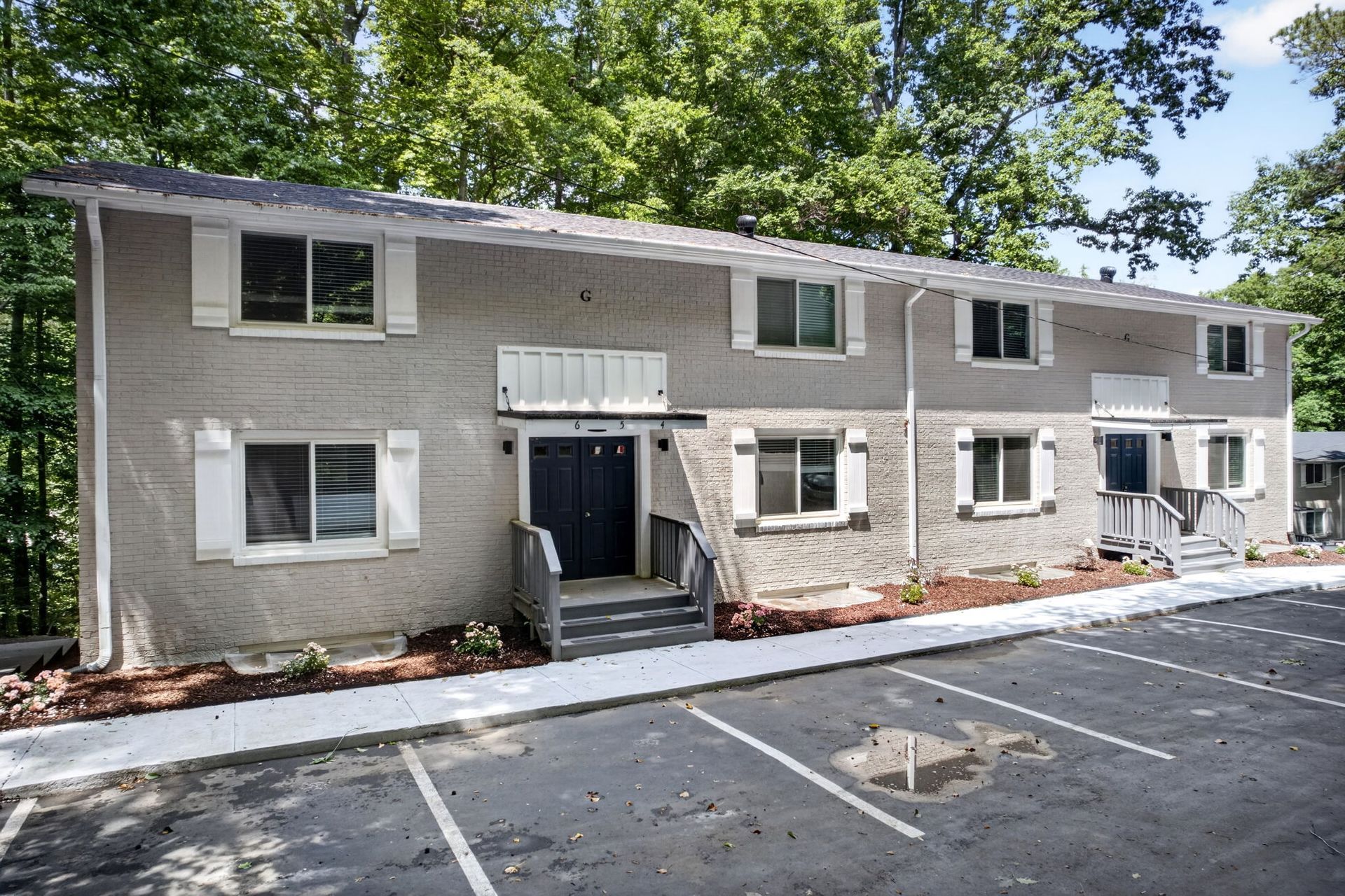 Two-story beige apartment building with white shutters and parking spaces in front