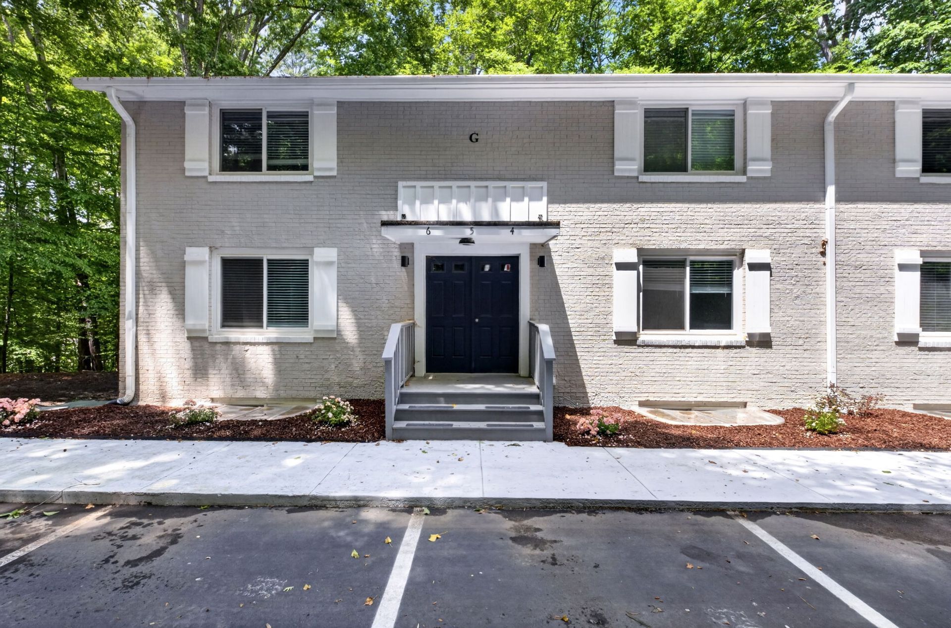 Apartment building entrance with black door, steps, and parking spaces in front