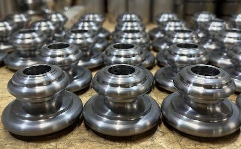 Close-up of many machined metal parts with a round base, a central cylinder, and concentric rings.